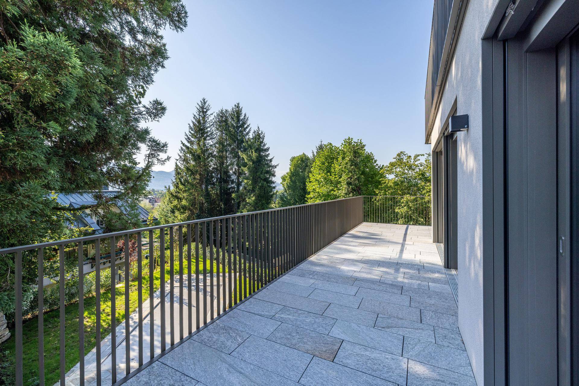 Geräumiger Balkon mit Steinplatten und weitem Blick ins Grüne sowie auf die Berge.