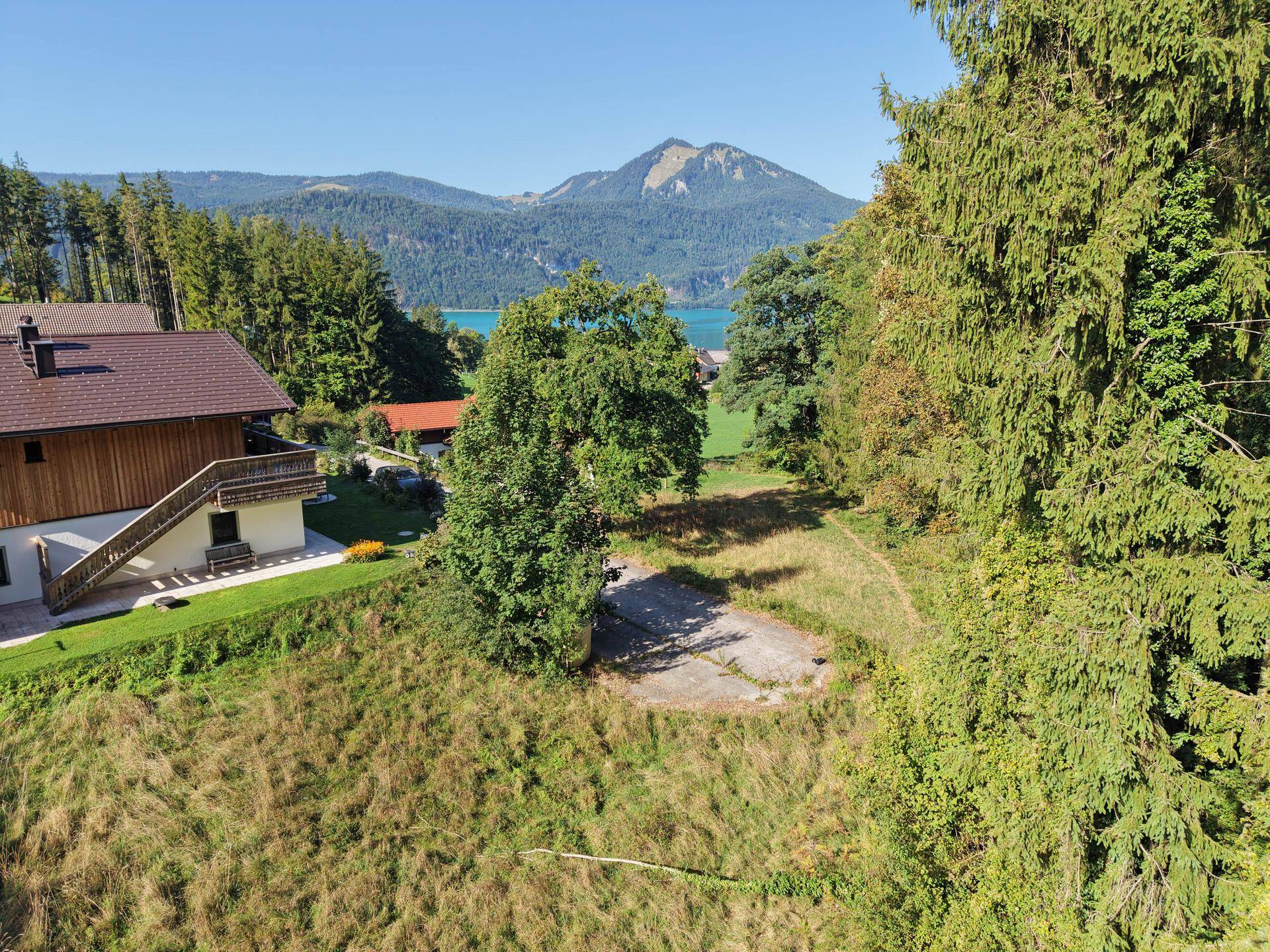 Luftaufnahme eines Hauses mit großem Grundstück, Wald und einem See in der Ferne.