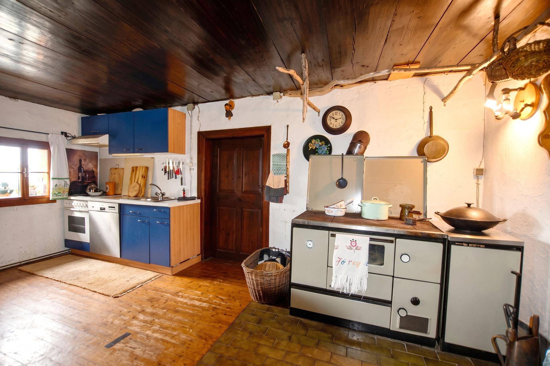 Rustikale Küche mit blauen Schränken, Holzofen und einer Kombination aus Holzdielen- und Fliesenboden.