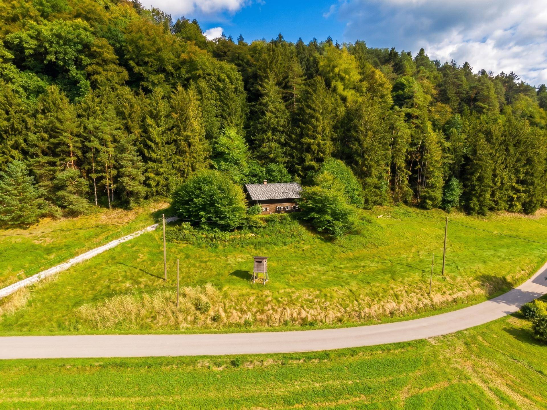 Luftaufnahme eines abgelegenen Chalets, eingebettet in eine grüne Waldlandschaft mit Wiesen und Wegen.