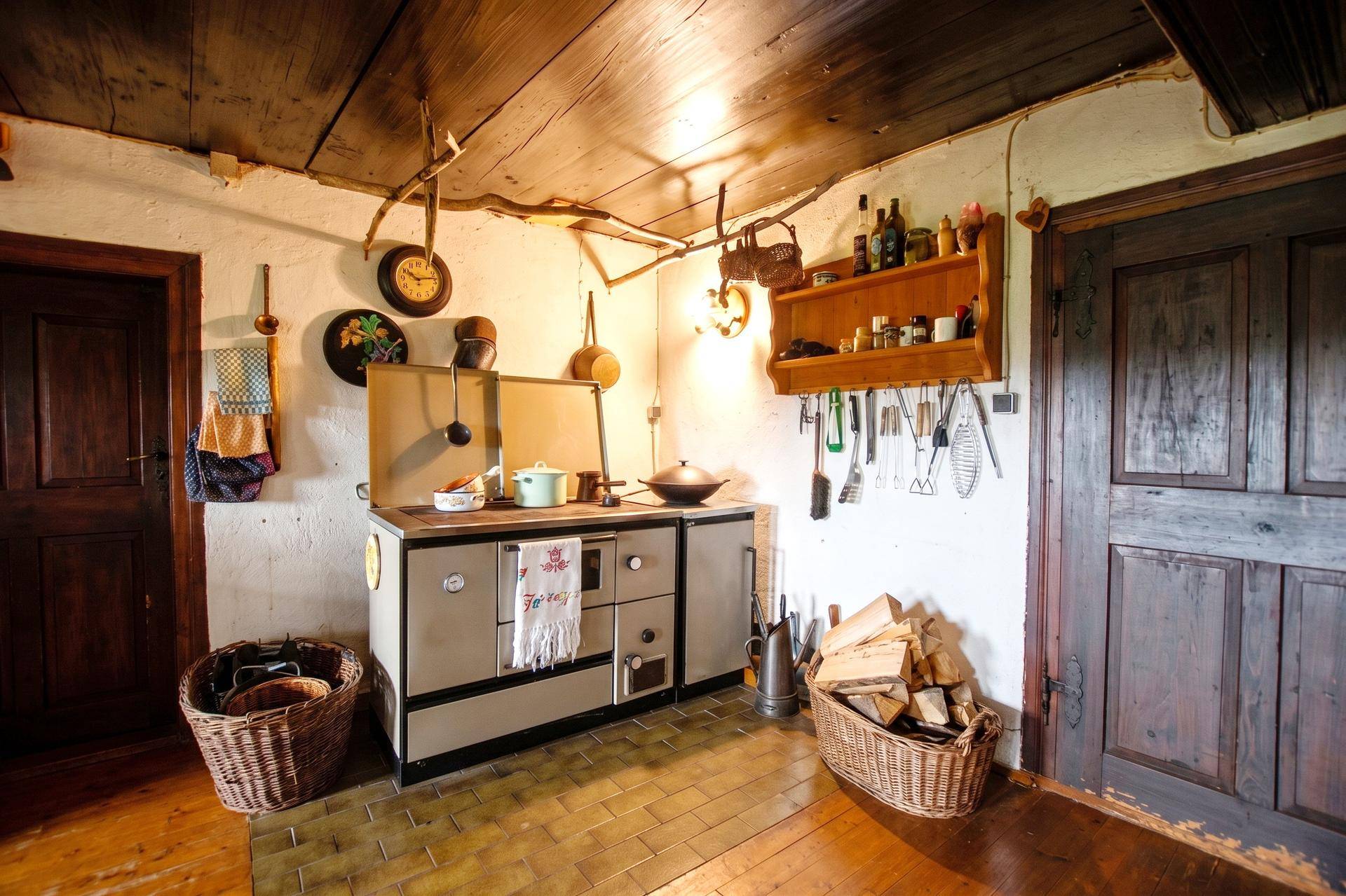 Gemütliche rustikale Küche mit traditionellem Holzofen, gefliestem Boden und Holzbalkendecke.