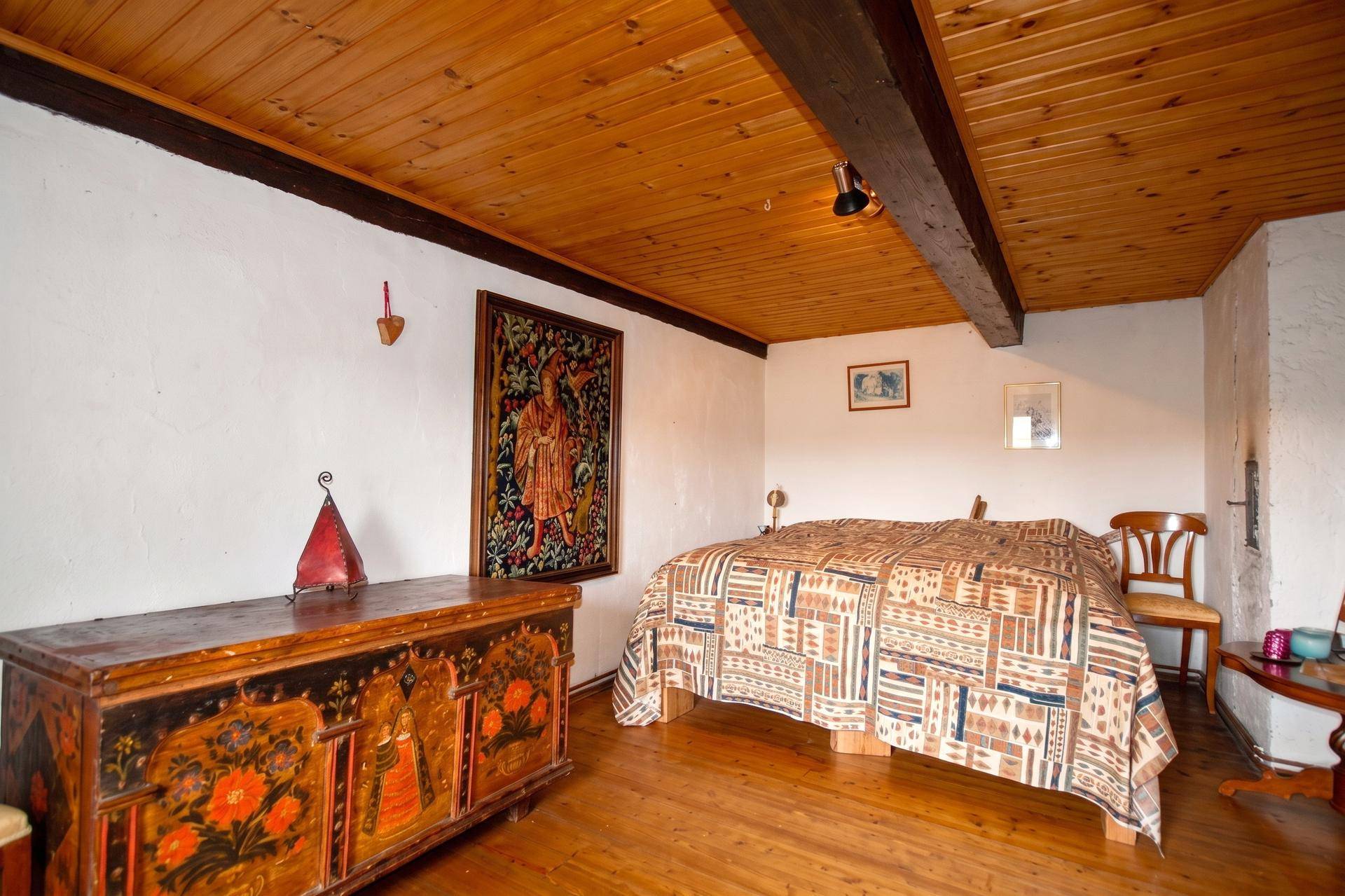 Gemütliches Schlafzimmer mit Holzdielenboden, sichtbaren Deckenbalken und einer bemalten Truhe.