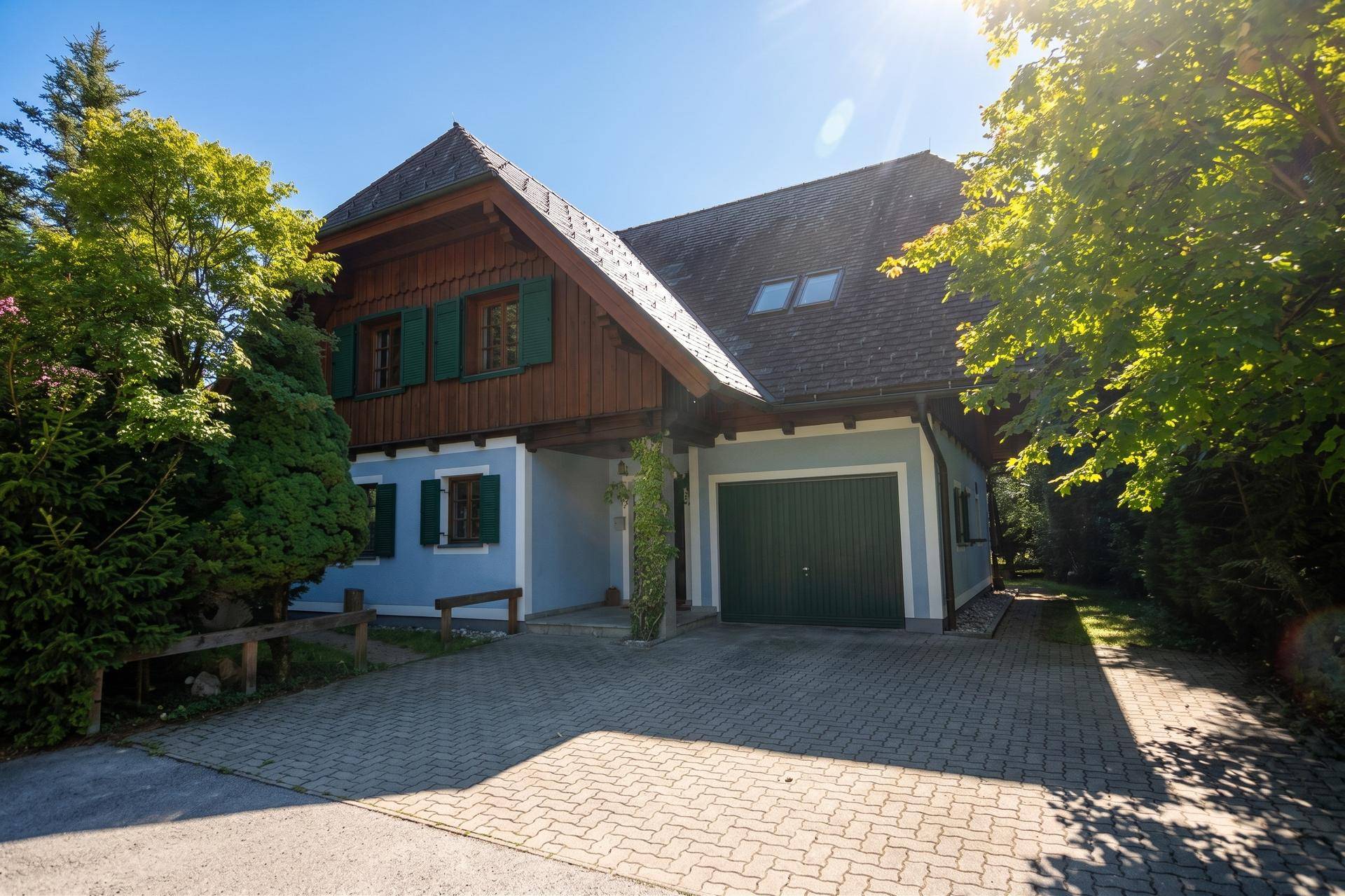 Hausfront mit integrierter Garage, gepflasterter Auffahrt und grünen Fensterläden.