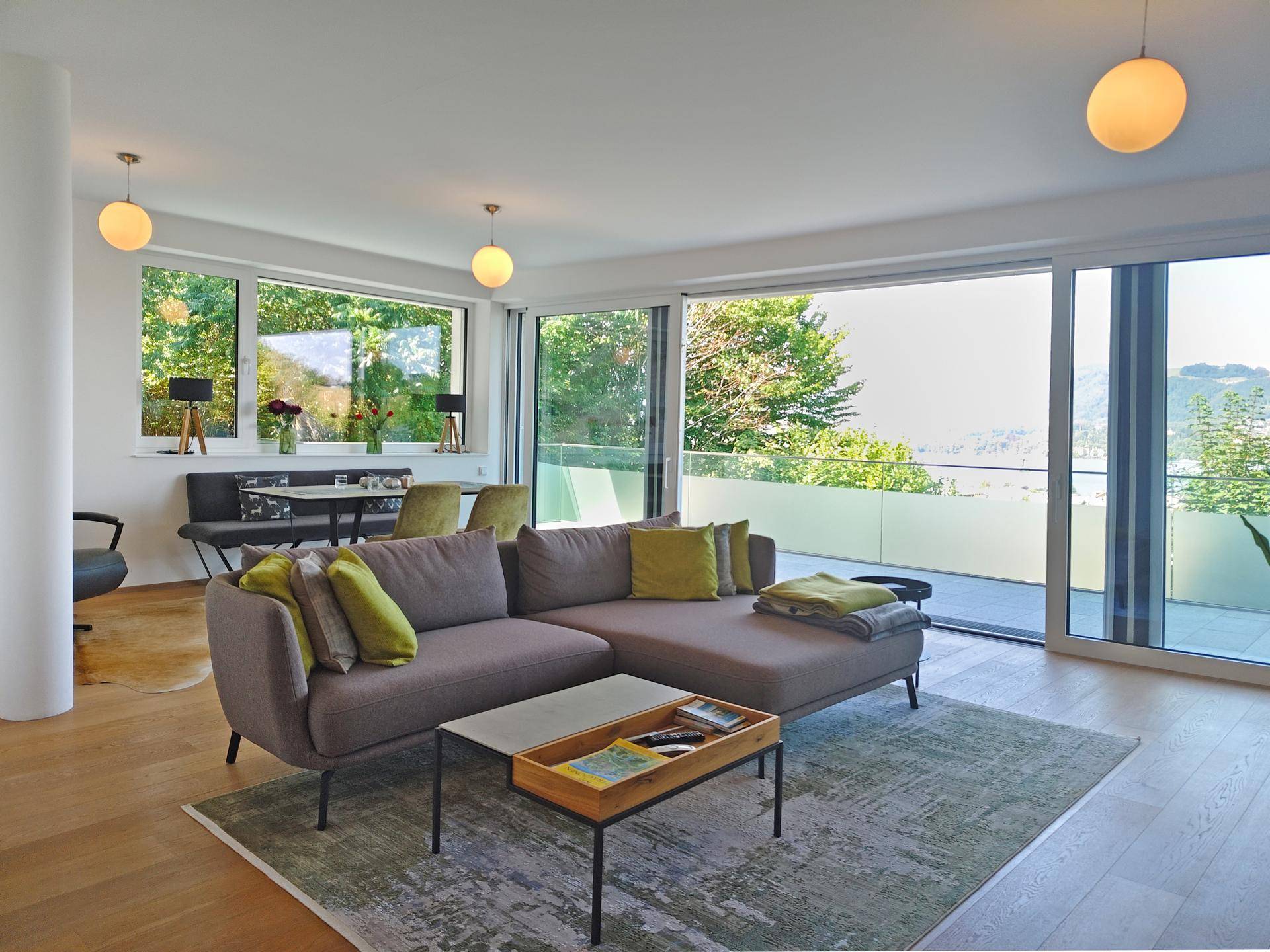 Helles Wohnzimmer mit modernem Sofa, Holzboden und Zugang zu einer großen Terrasse mit Weitblick.