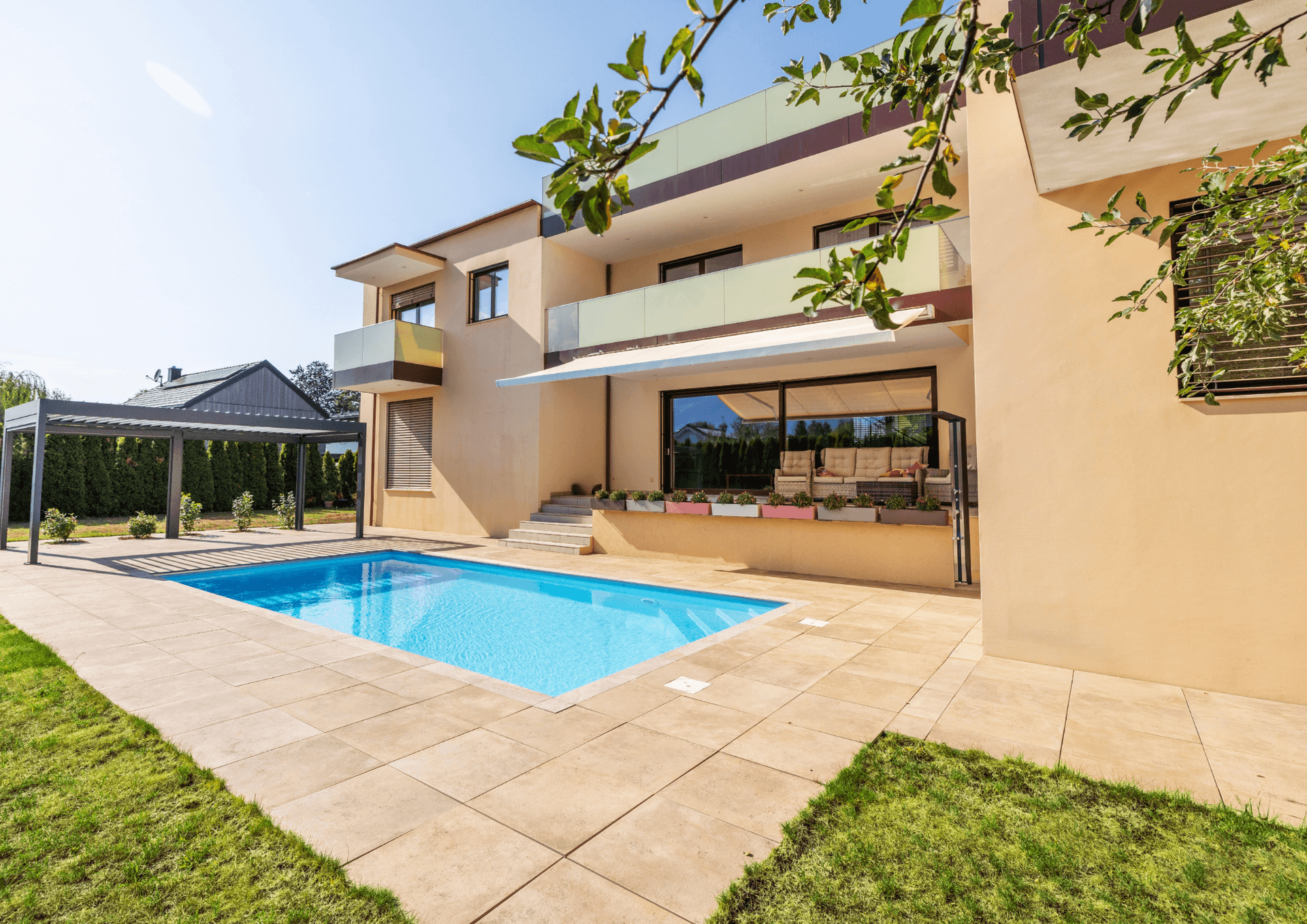 Großzügiger Poolbereich mit Terrasse und Pergola vor der modernen Hausfassade.