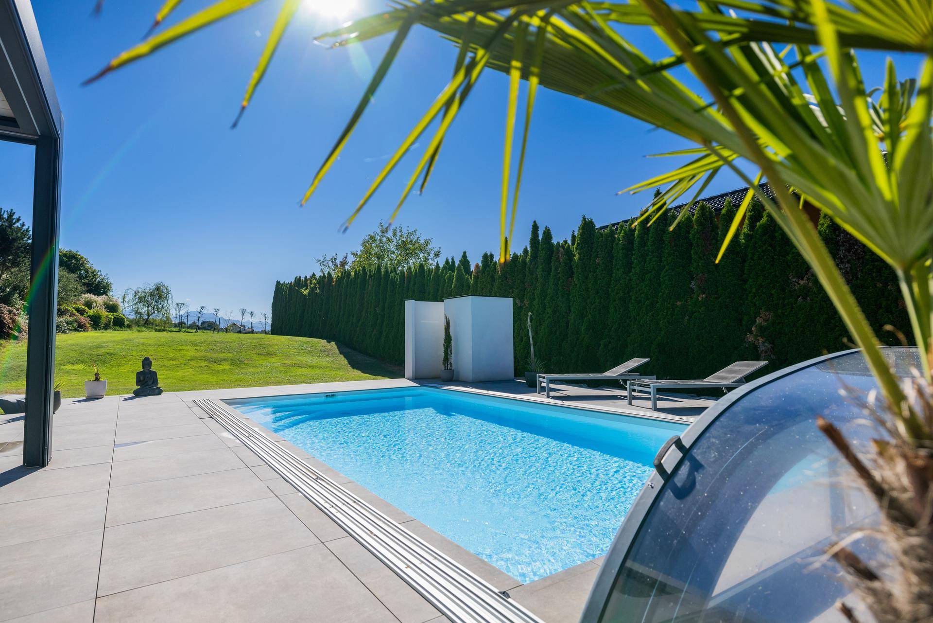 Weitläufiger Poolbereich mit Liegestühlen und üppiger Vegetation unter strahlend blauem Himmel.