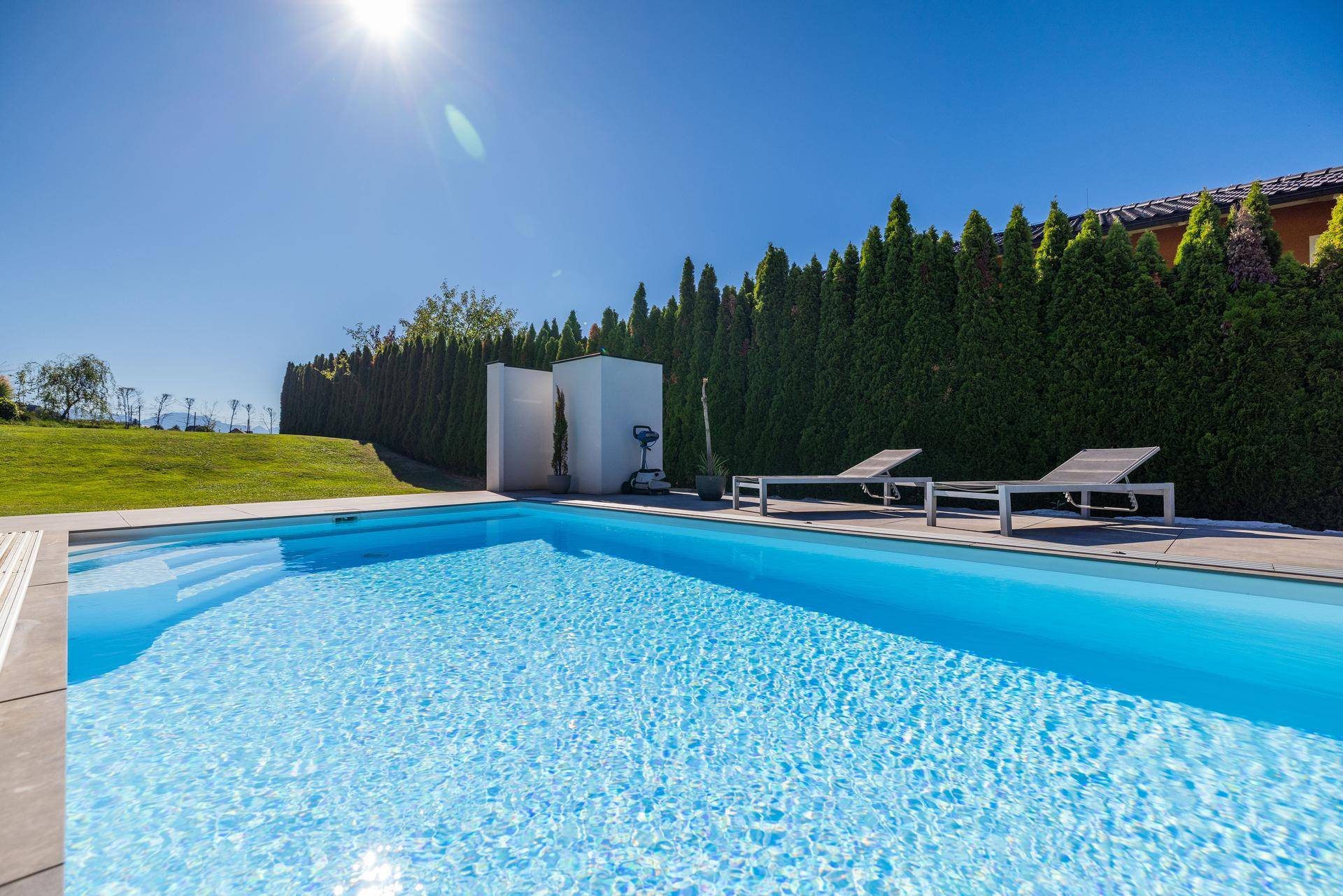 Großer, sonniger Poolbereich mit Liegestühlen und hoher Hecke für Privatsphäre im Garten.