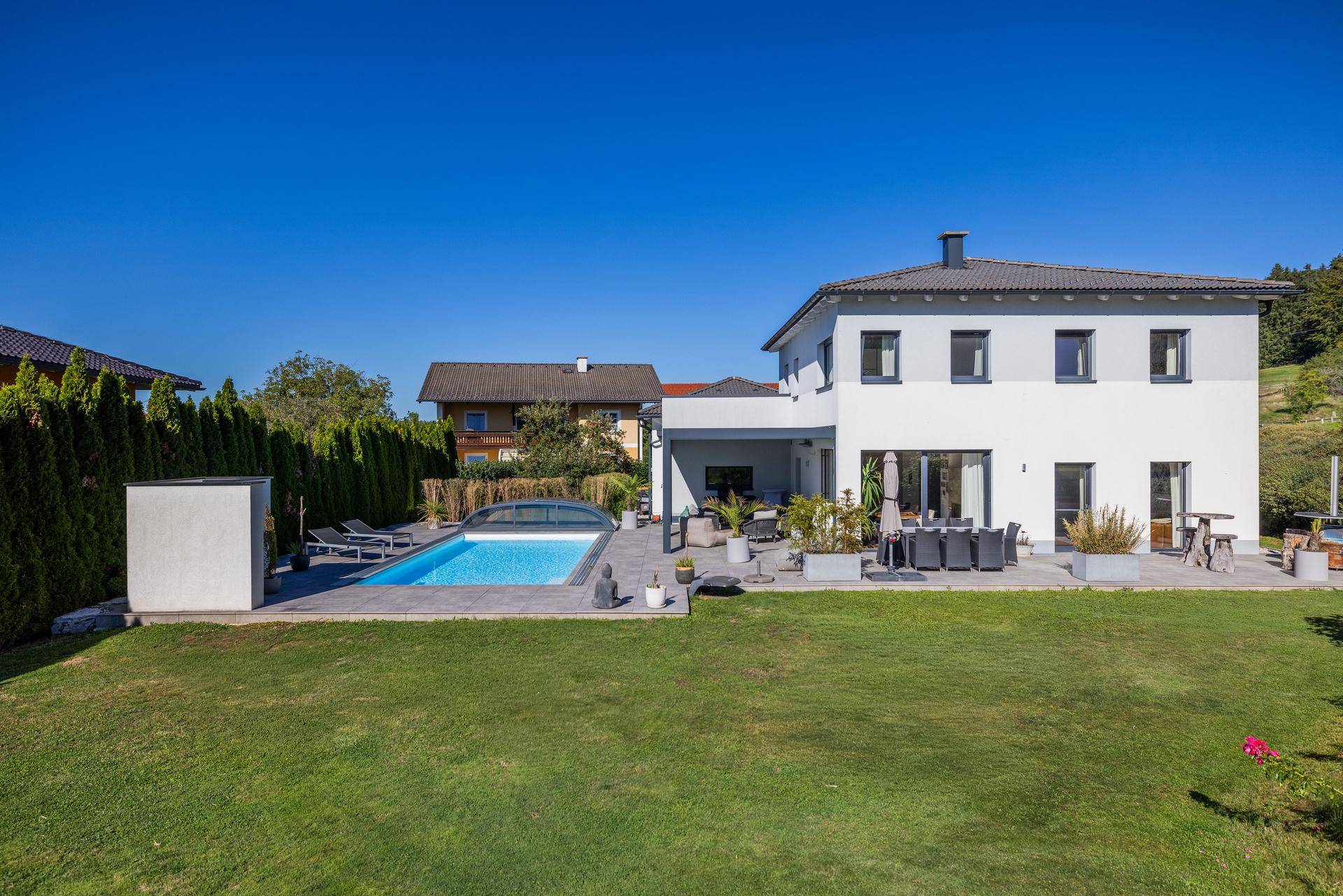 Weitläufiger Gartenbereich mit Rasenfläche, Pool und modernem Einfamilienhaus im Hintergrund.