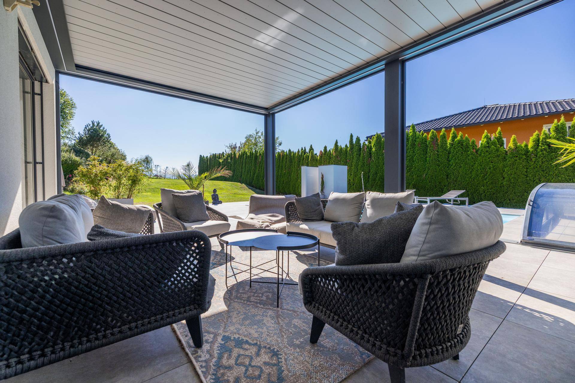 Gemütliche, überdachte Terrasse mit modernen Lounge-Möbeln und Blick auf den Garten und Pool.