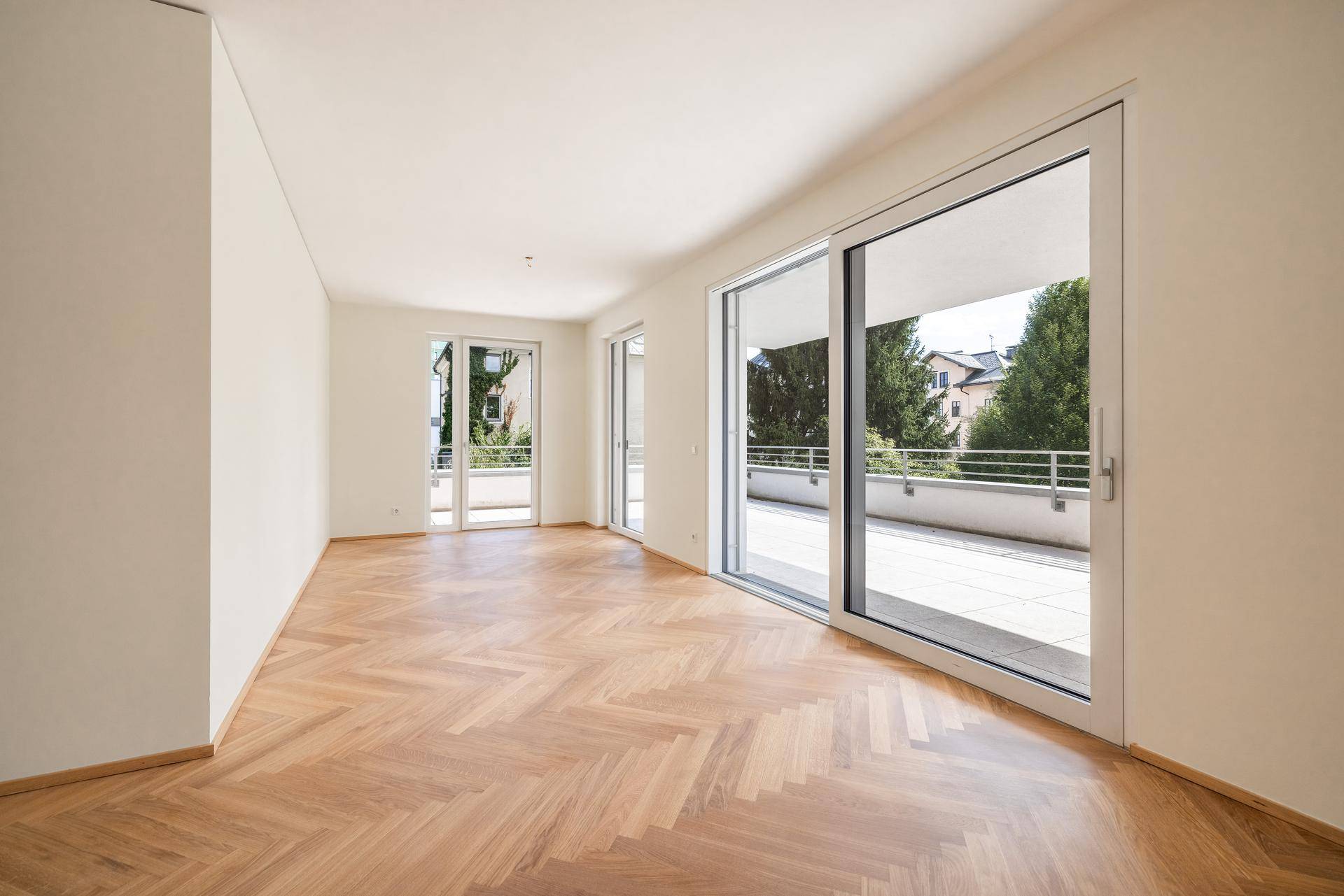 Heller Wohnraum mit Fischgrätparkett und großem Schiebefenster zur Terrasse.