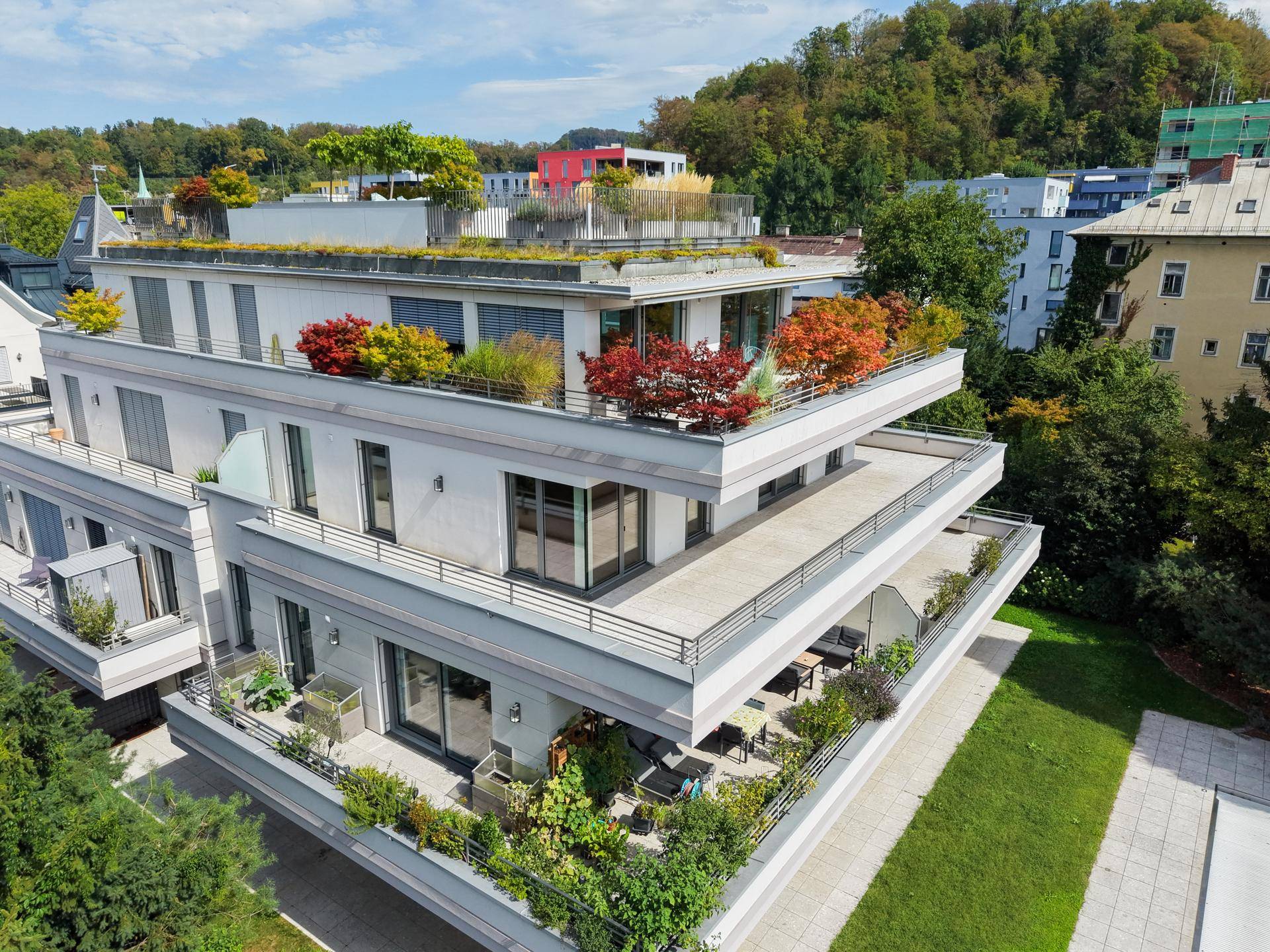 Modernes Wohngebäude mit mehreren Terrassen und begrüntem Dach in städtischer Umgebung.
