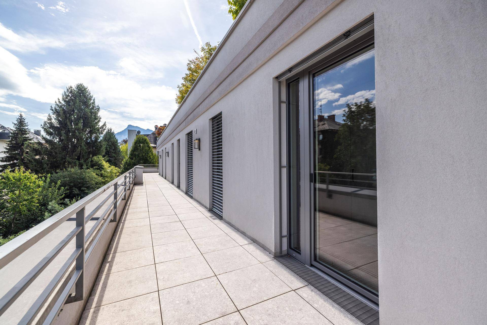 Lange, geflieste Terrasse mit moderner Balustrade und Blick auf die Umgebung.