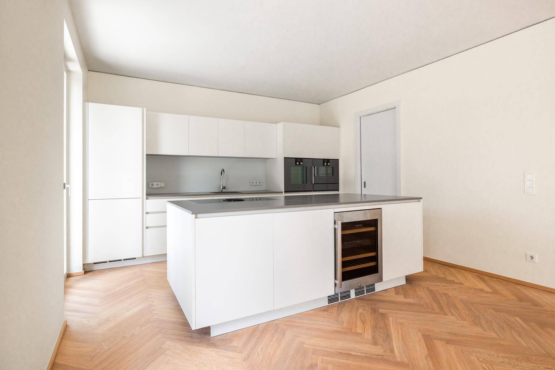 Moderne Einbauküche mit weißer Front, Kücheninsel und integriertem Weinkühler.