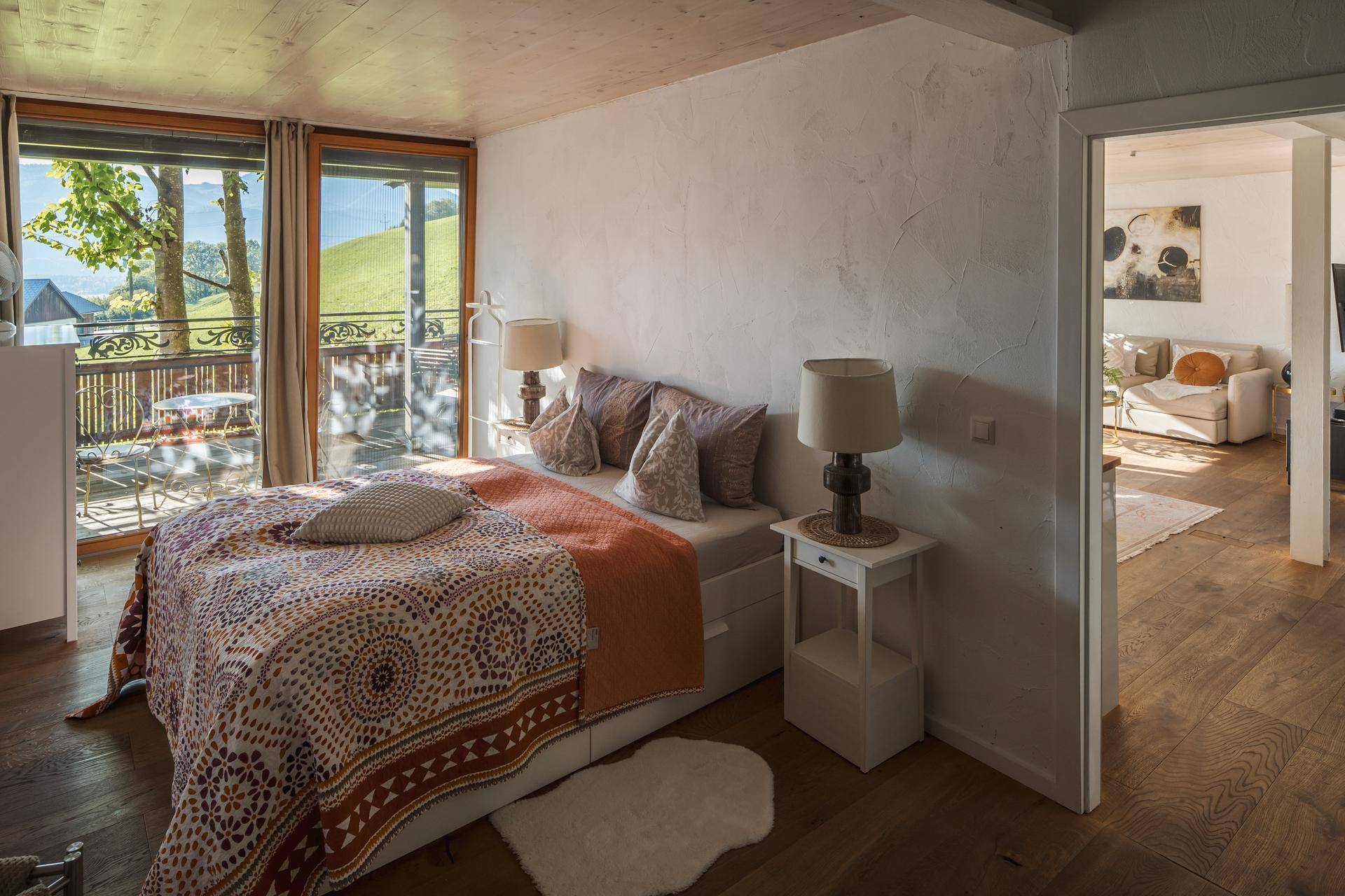 Helles Schlafzimmer mit Doppelbett, Holzboden und Zugang zu einem Balkon mit grüner Aussicht.