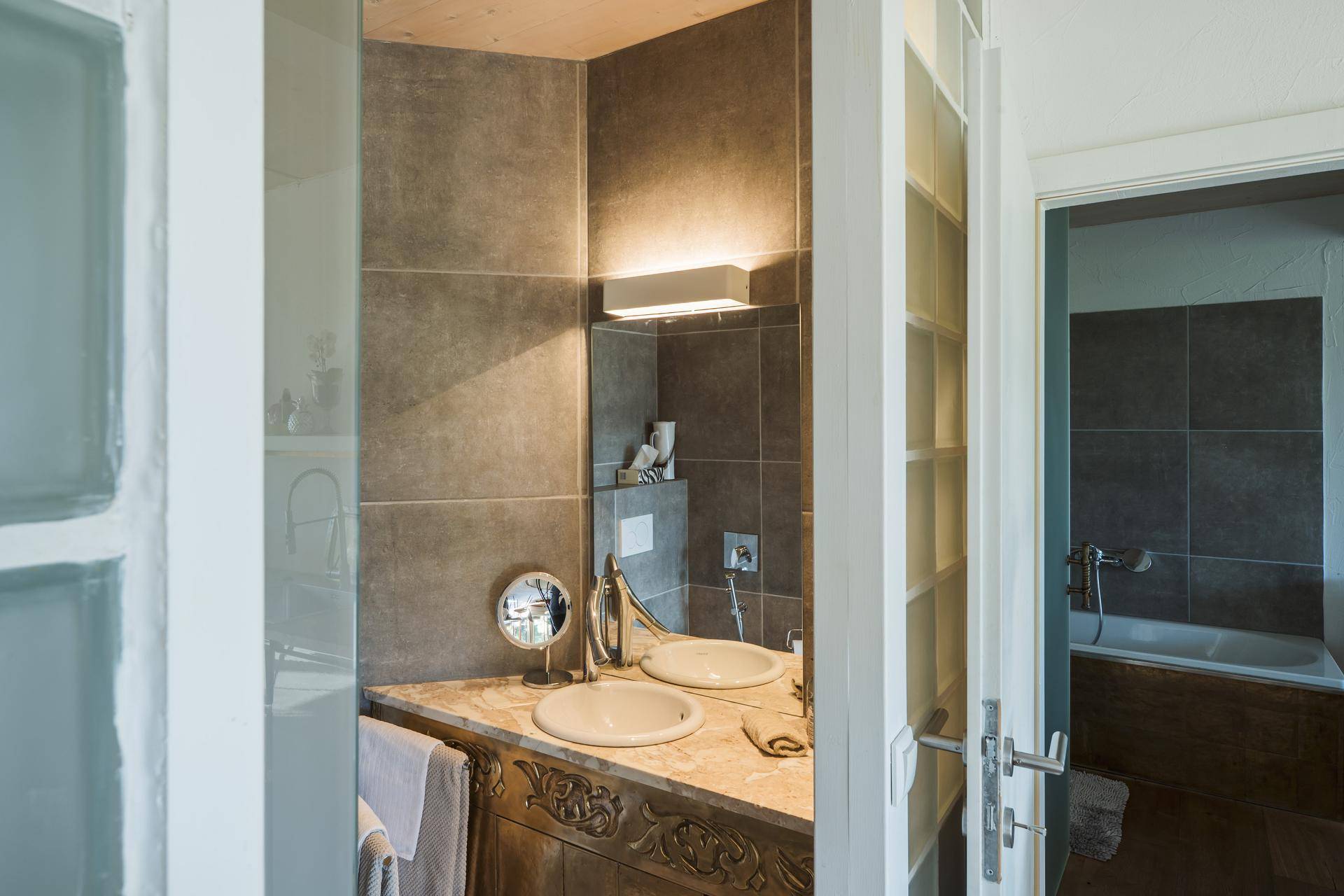 Modernes Badezimmer mit Einzelwaschbecken, großem Spiegel und grauen Fliesen.