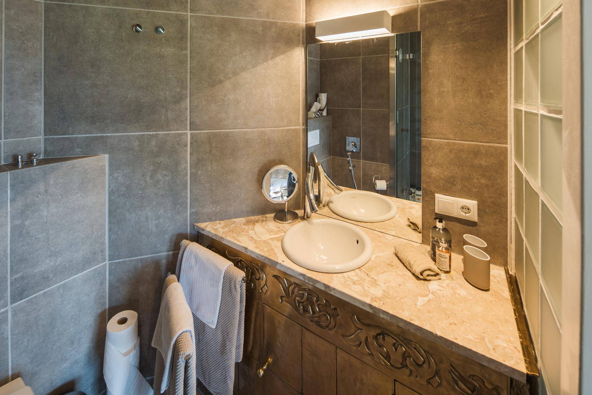 Elegantes Badezimmer mit Waschtisch, Spiegel und modernen grauen Fliesen an den Wänden.