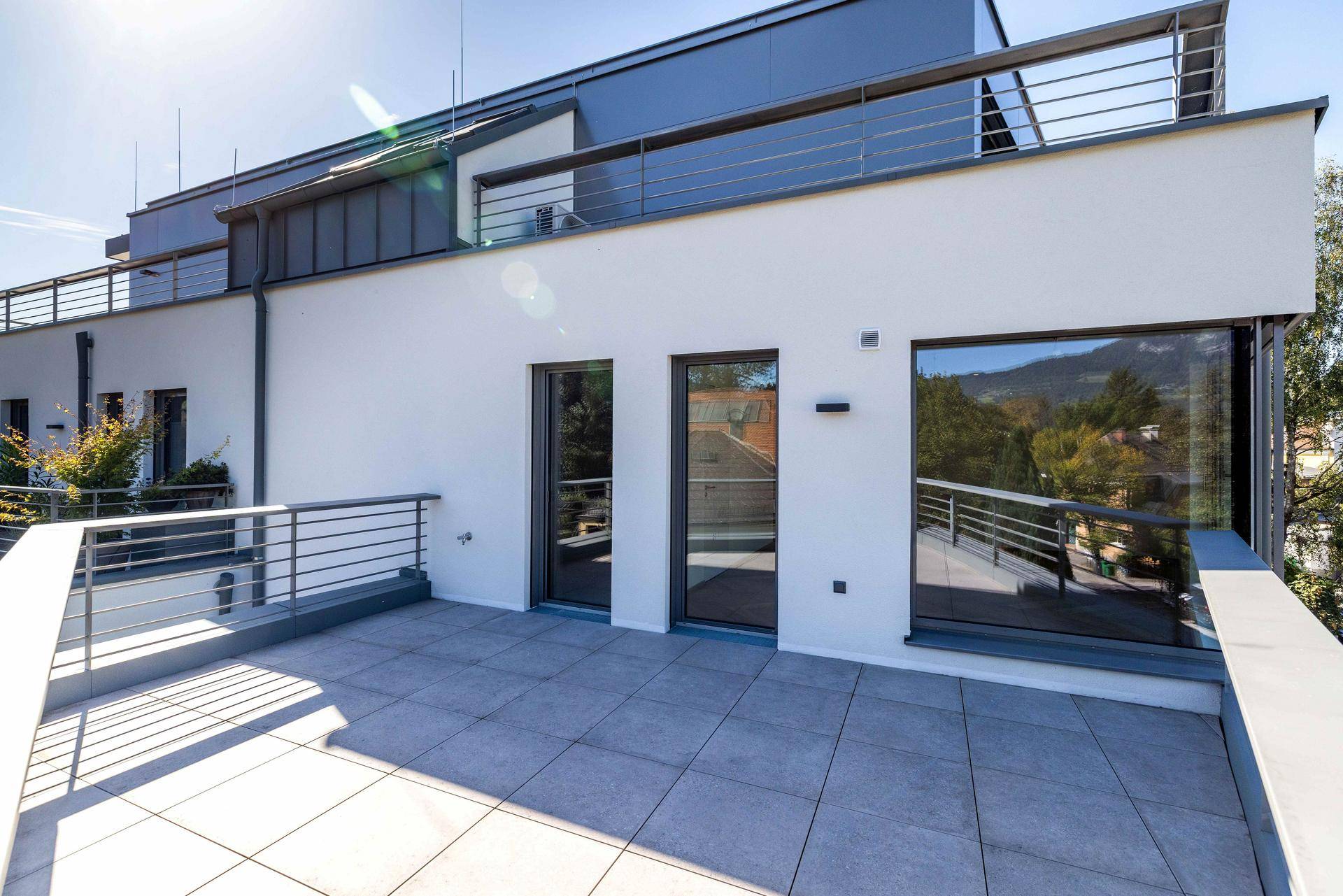 Weiße Gebäudefassade mit mehreren Terrassenbereichen und großen Fenstern, die viel Licht hereinlassen.