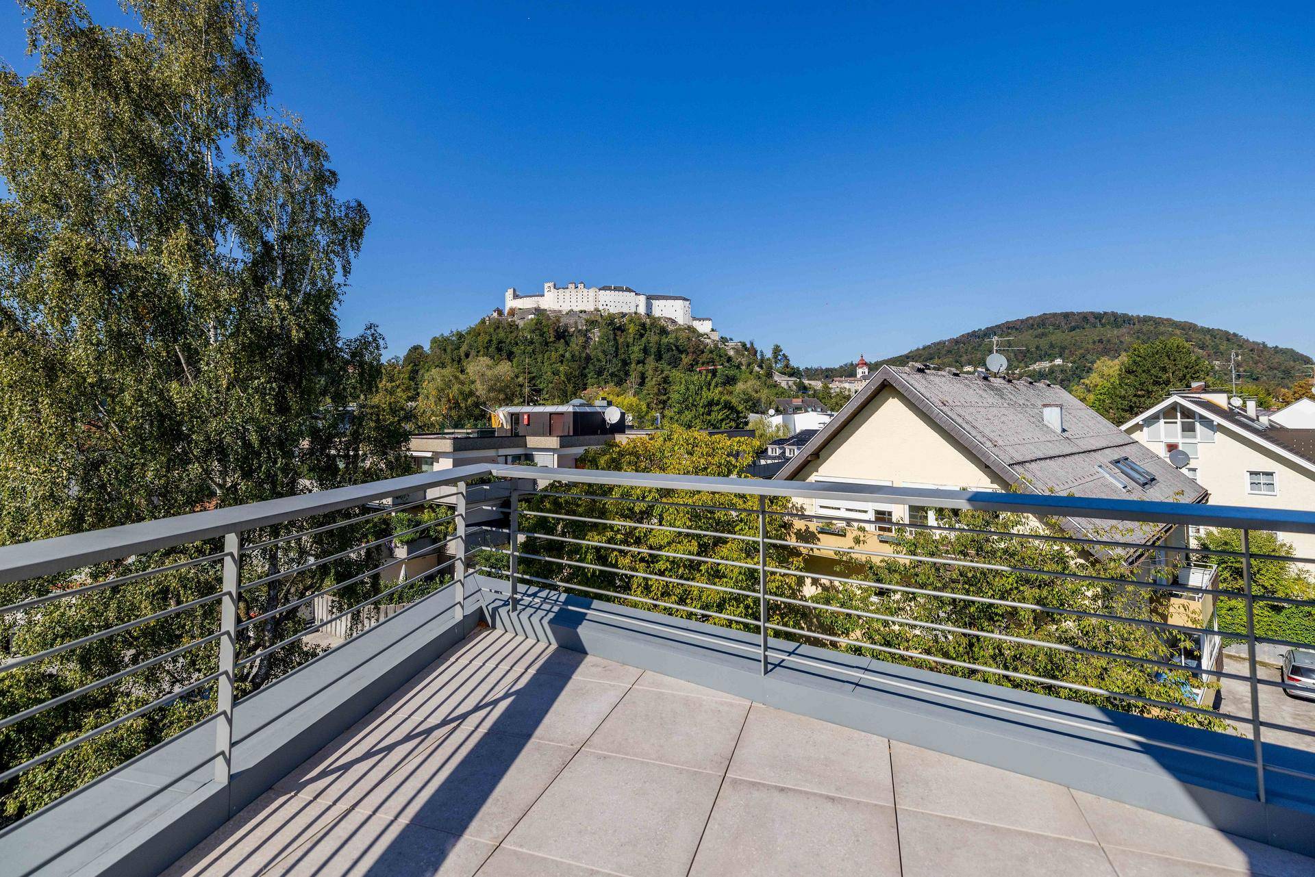 Sonniger Terrassenbereich mit Metallgeländer und Panoramablick auf die Stadt und die Festung Hohensalzburg.