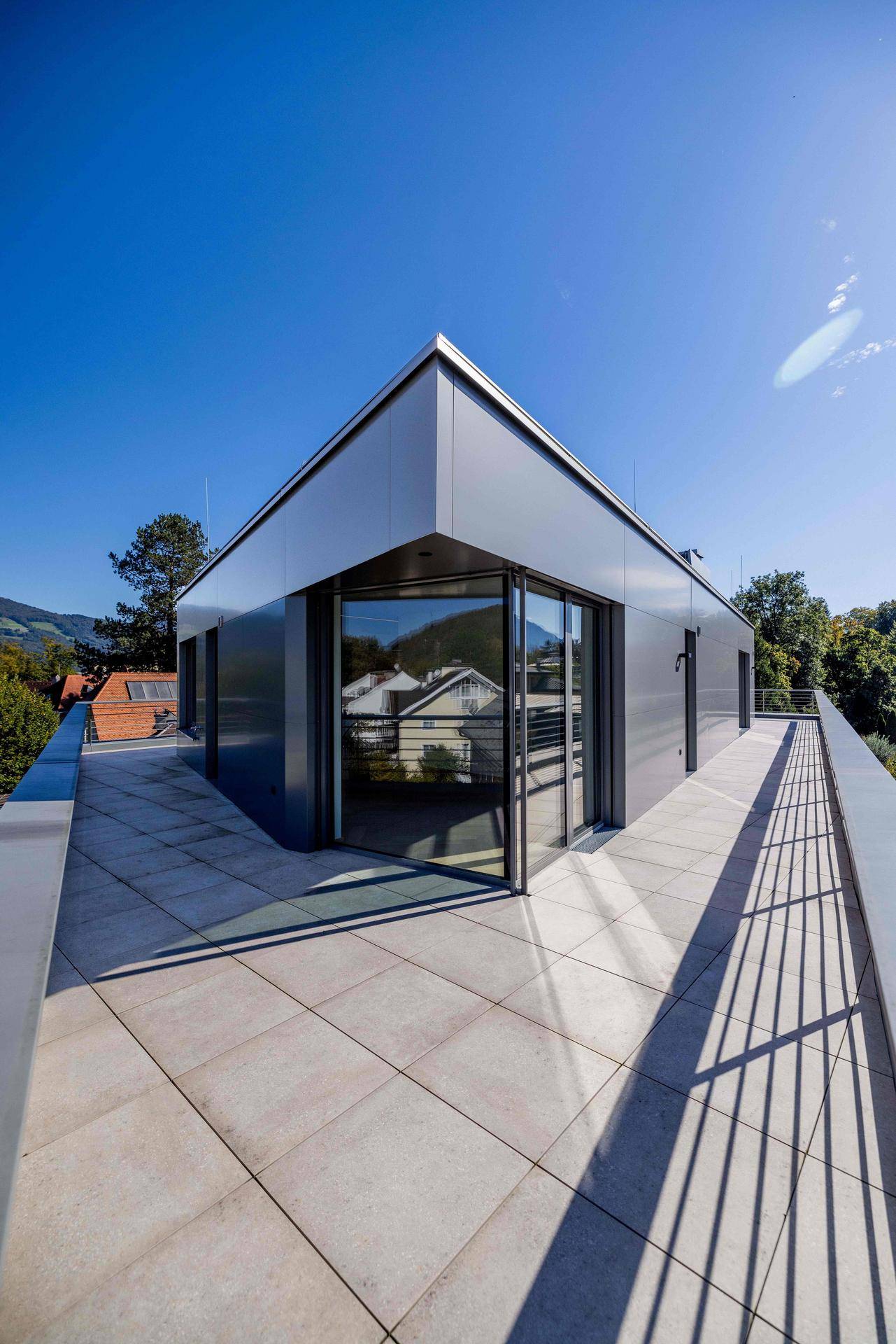 Moderne Gebäudefassade mit großen Glasflächen und einer weitläufigen Dachterrasse unter klarem Himmel.