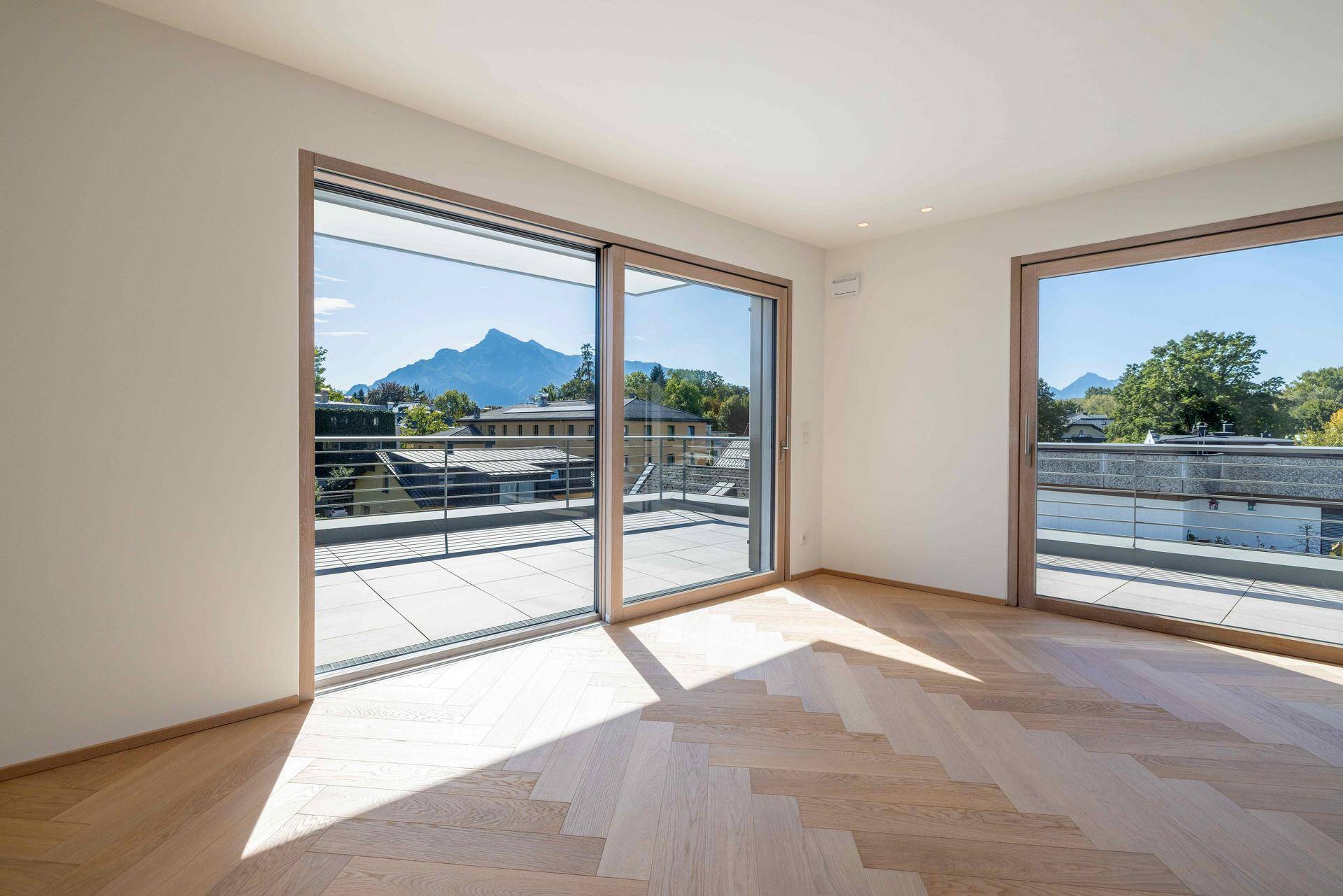 Lichtdurchfluteter Raum mit Holzparkett und Schiebetüren, die Zugang zu einer Terrasse mit Bergblick bieten.