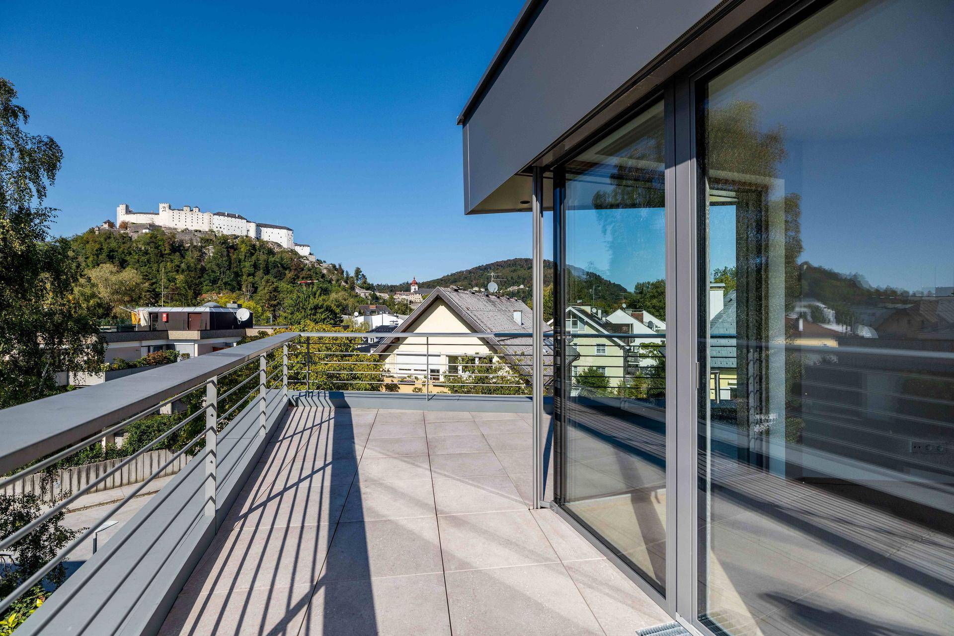 Geräumige Dachterrasse mit Fliesenboden und Blick auf die Stadt und die historische Festung Hohensalzburg.