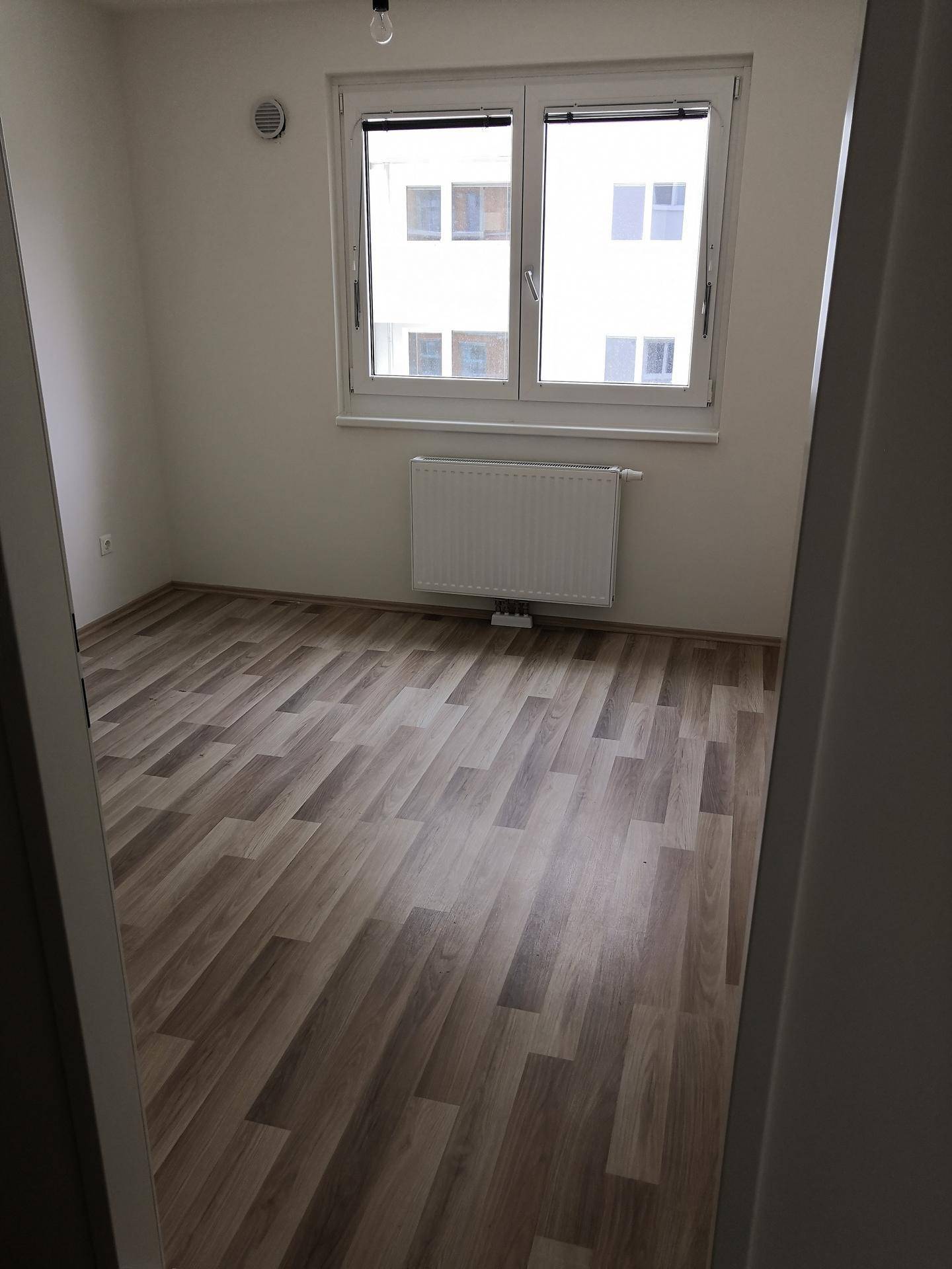 Helles Zimmer mit Laminatboden und großem Fenster, bereit zur Einrichtung.
