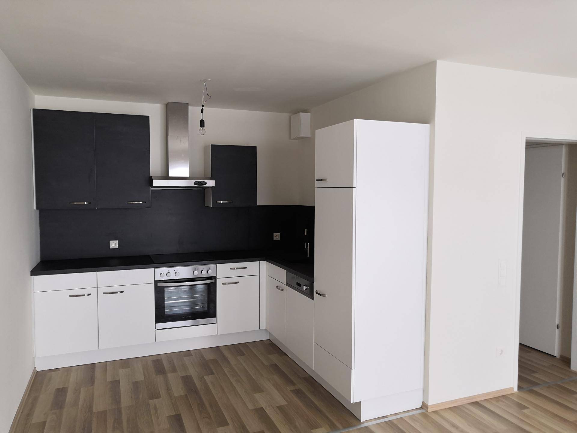 Neue Einbauküche mit weißen Unterschränken, dunklen Oberschränken und Laminatboden.