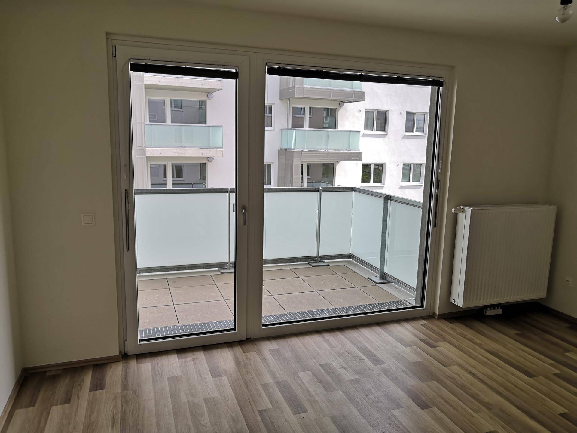 Heller Raum mit Laminatboden und Zugang zu einem Balkon mit Glasbrüstung.
