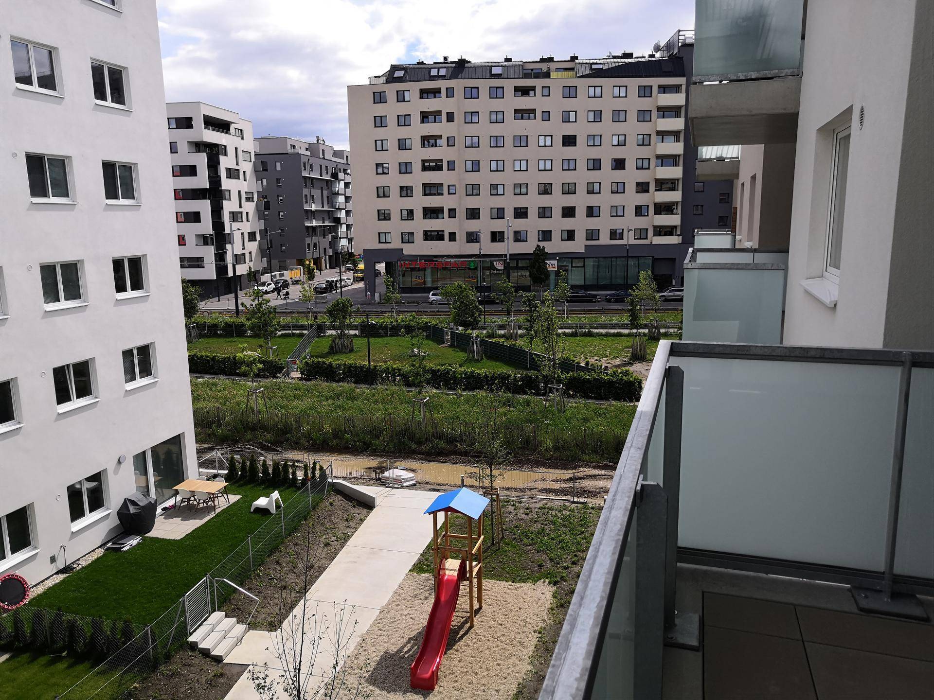 Blick vom Balkon auf eine Grünfläche mit Spielplatz und umliegende Wohngebäude.