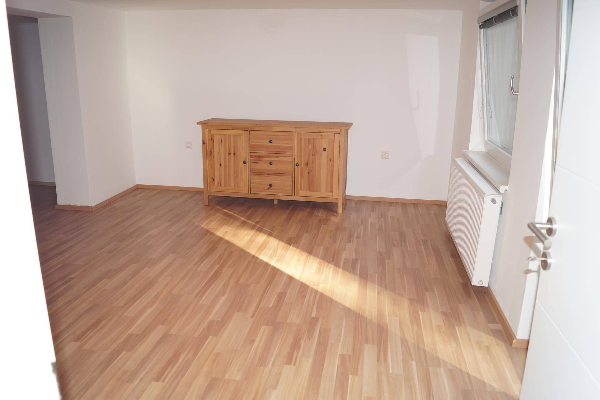 Helles Wohnzimmer mit Laminatboden, Holzkommode und viel natürlichem Sonnenlicht.