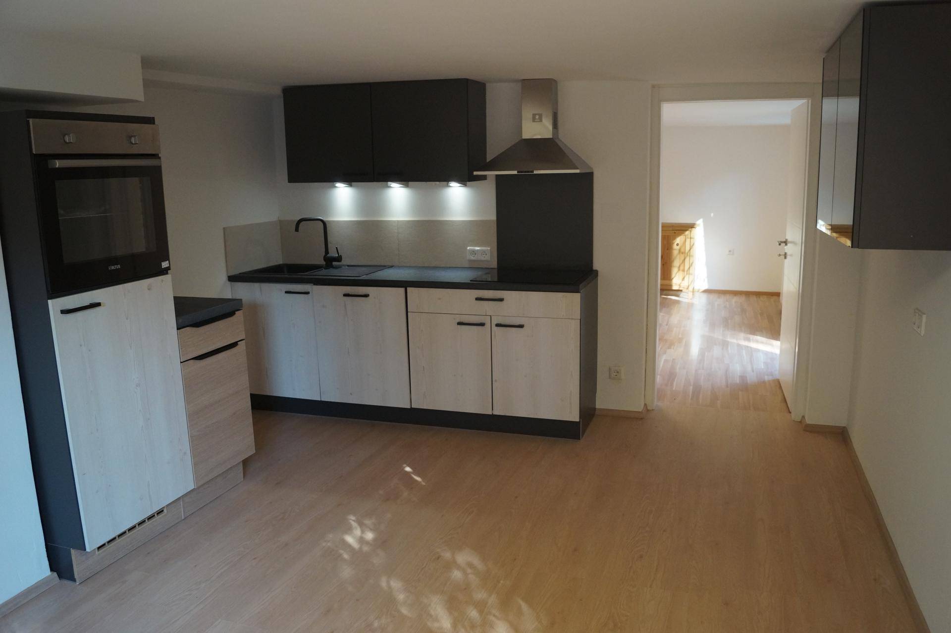 Geräumiger Küchenbereich mit moderner Einbauküche, Backofen und hellem Laminatboden.