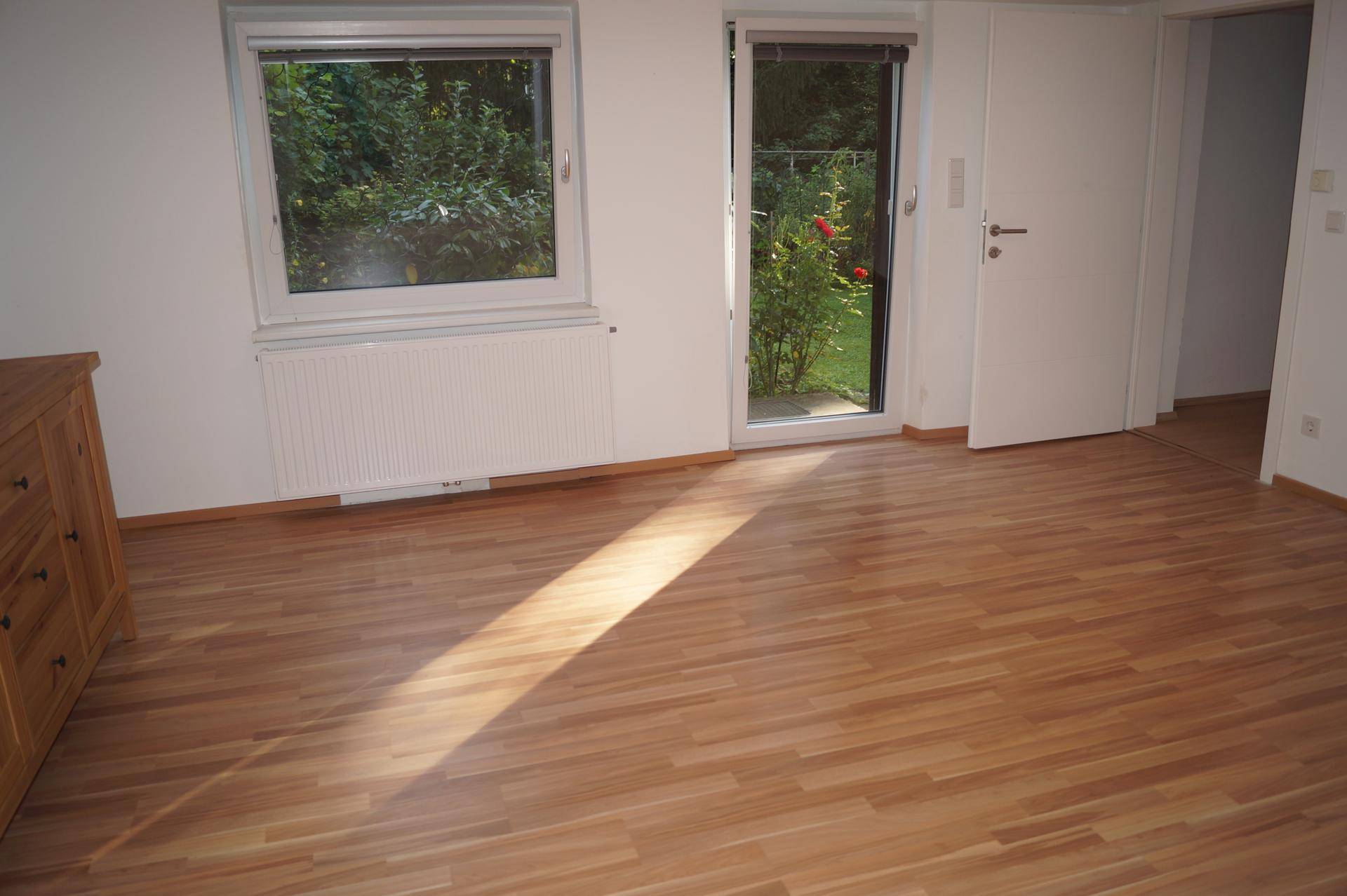 Wohnzimmer mit Laminatboden, Fenster und Glastür zum Garten, bietet viel Tageslicht.