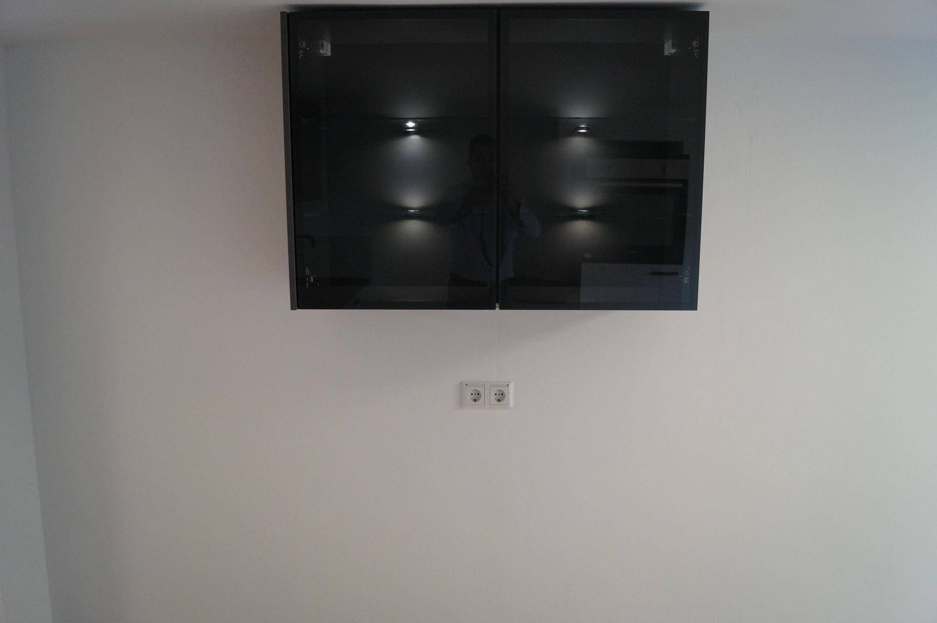 Zwei schwarze Hochglanz-Wandschränke mit integrierter Beleuchtung an einer weißen Wand.