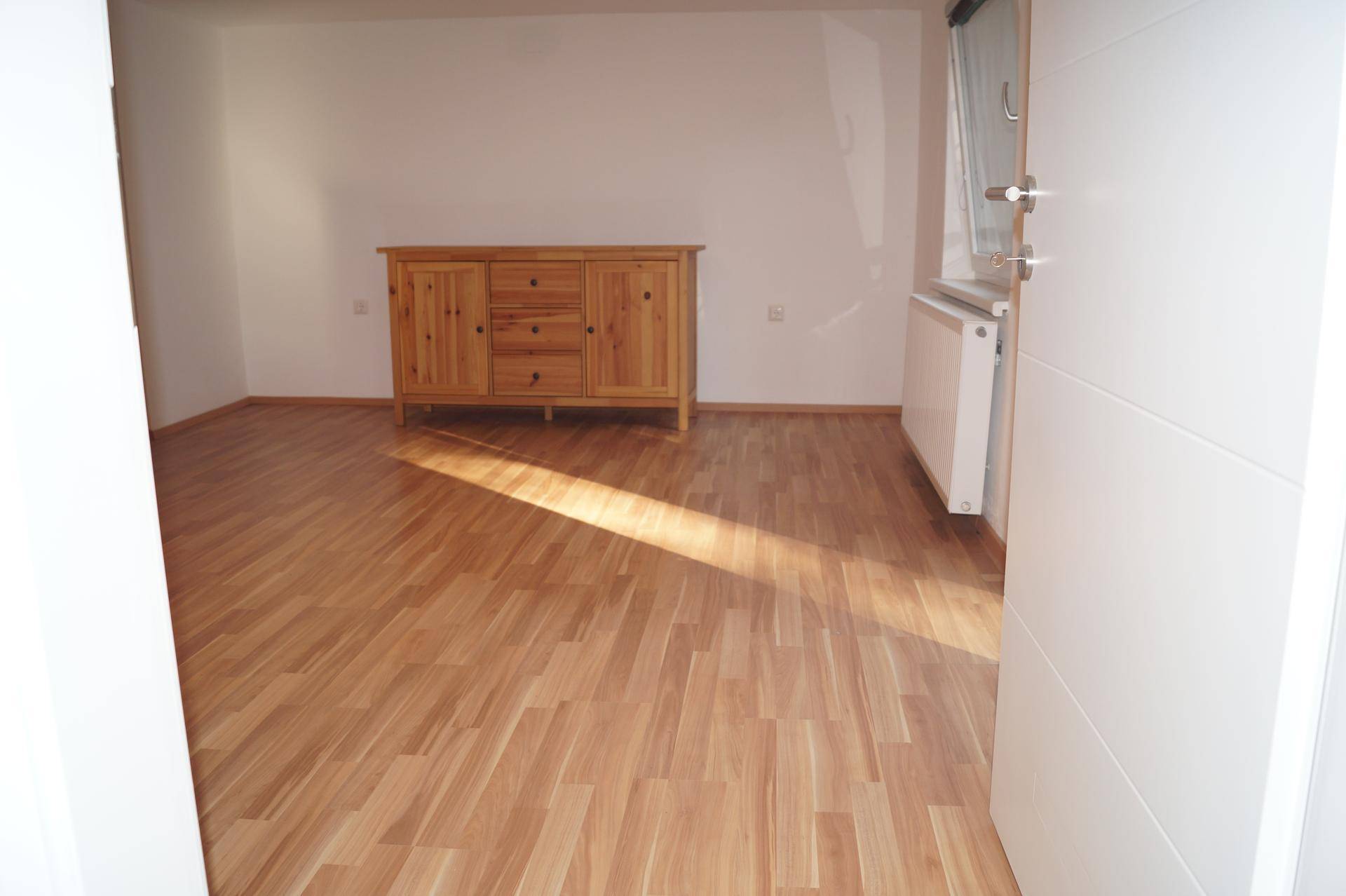 Lichtdurchflutetes Wohnzimmer mit Laminatboden und einer rustikalen Holzkommode.