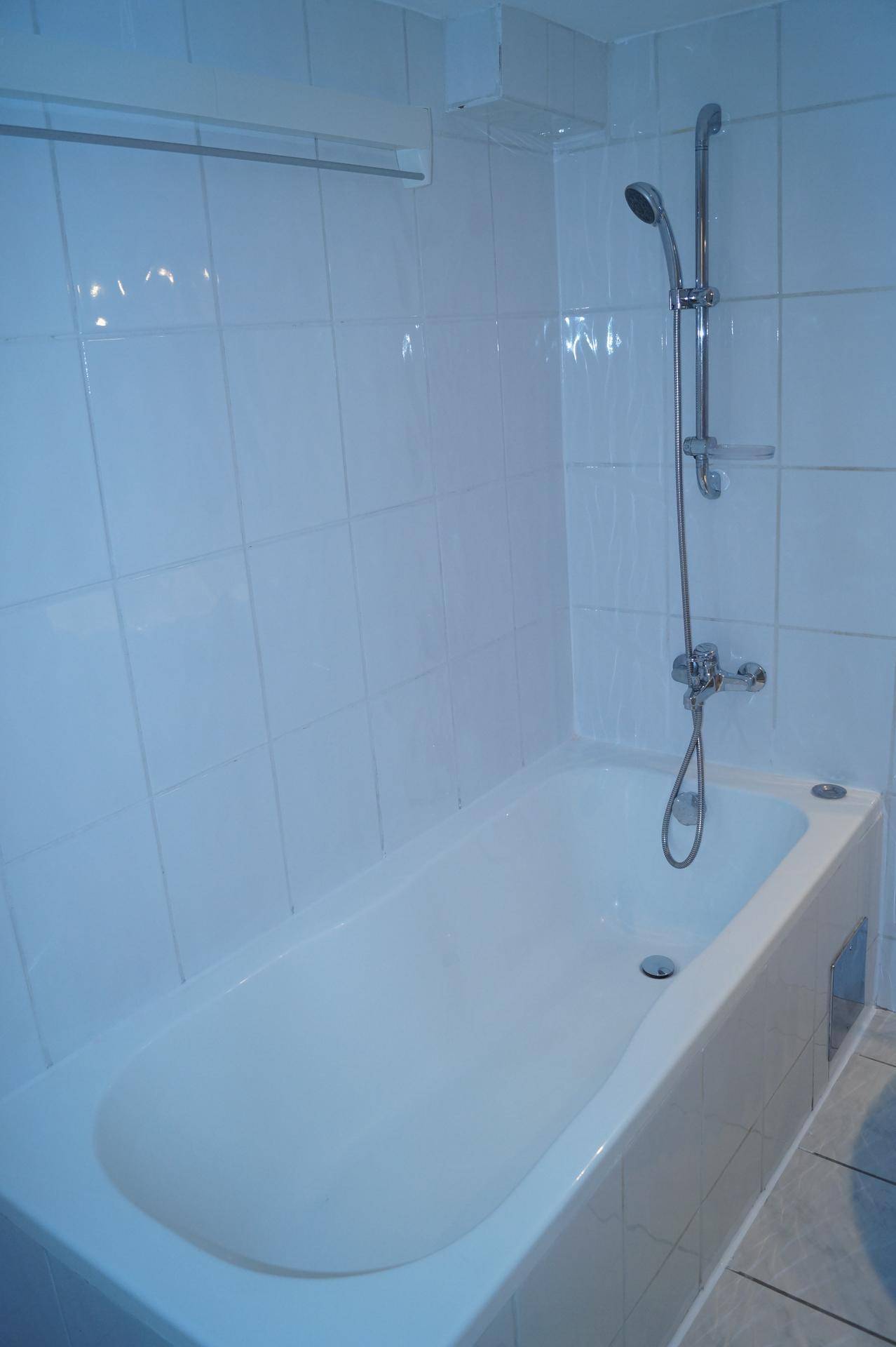 Badezimmer mit weißen Fliesen, Badewanne und Duschvorrichtung, funktional und hell.