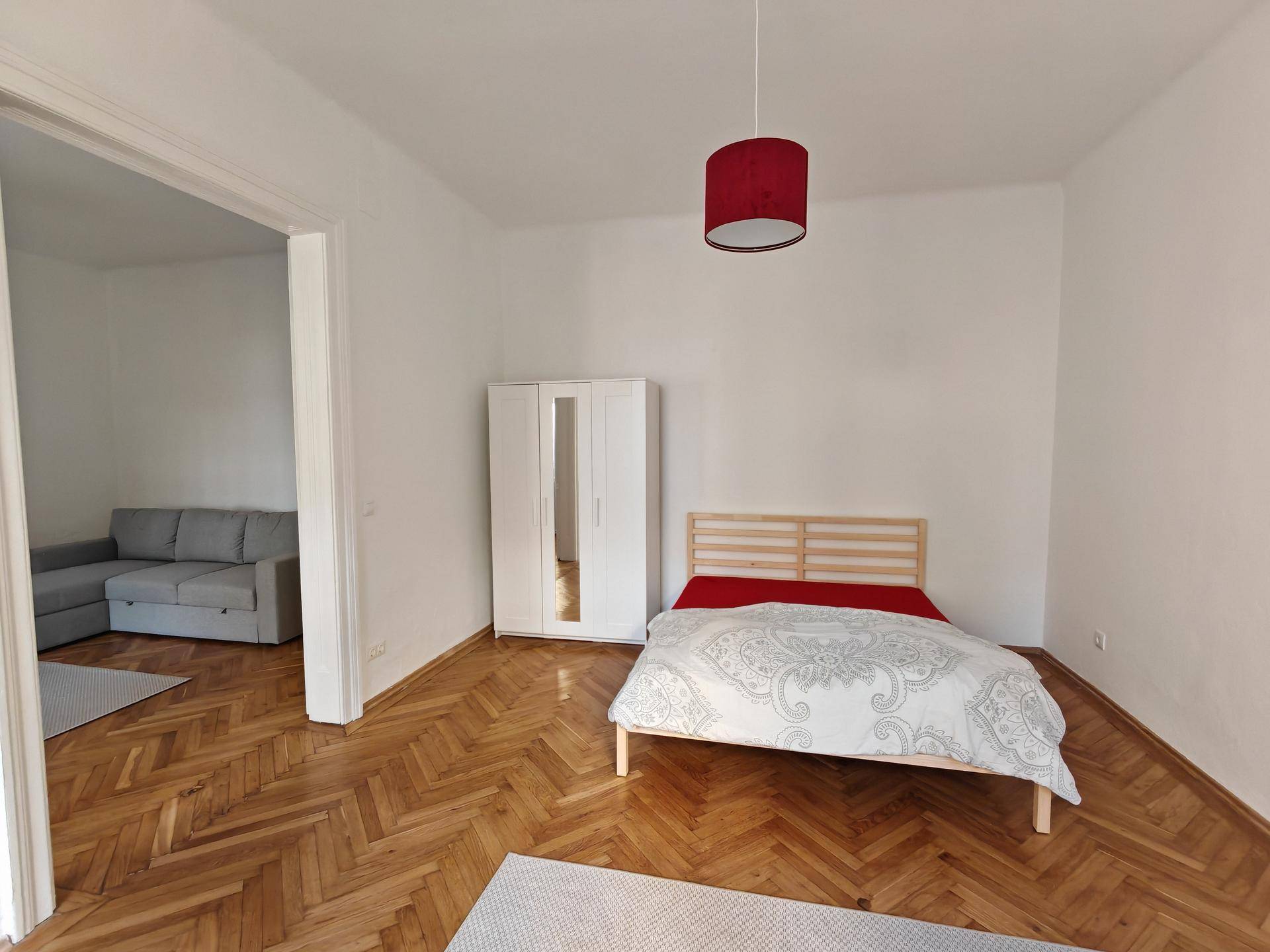 Schlafzimmer mit Holzbett, weißem Kleiderschrank und Zugang zum angrenzenden Wohnbereich.