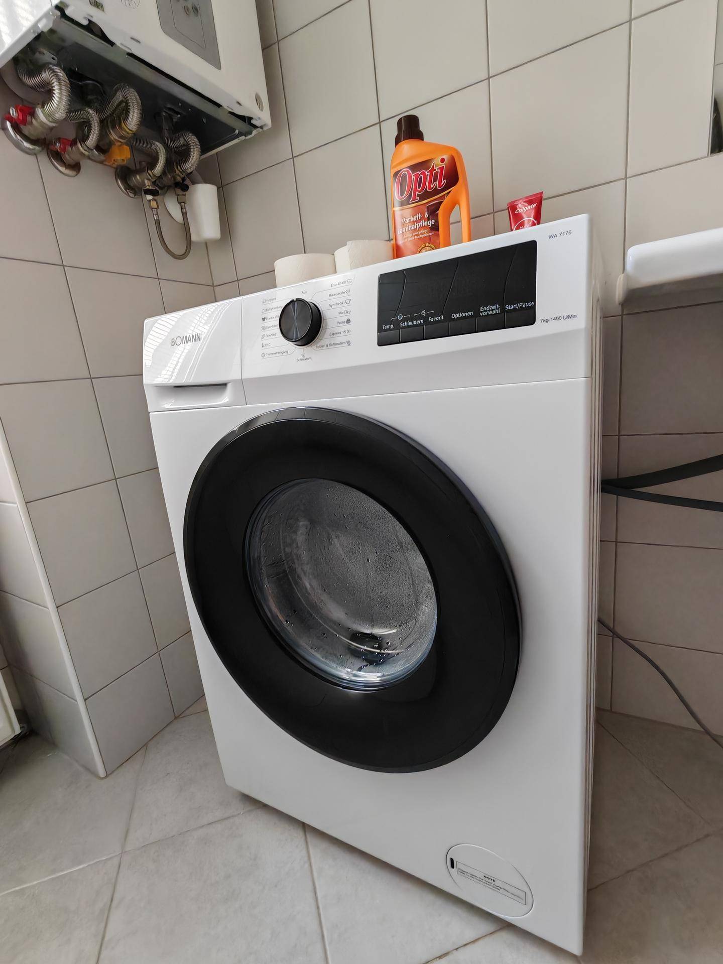 Nahaufnahme einer modernen Waschmaschine in einem gefliesten Badezimmer mit Warmwasserbereiter.