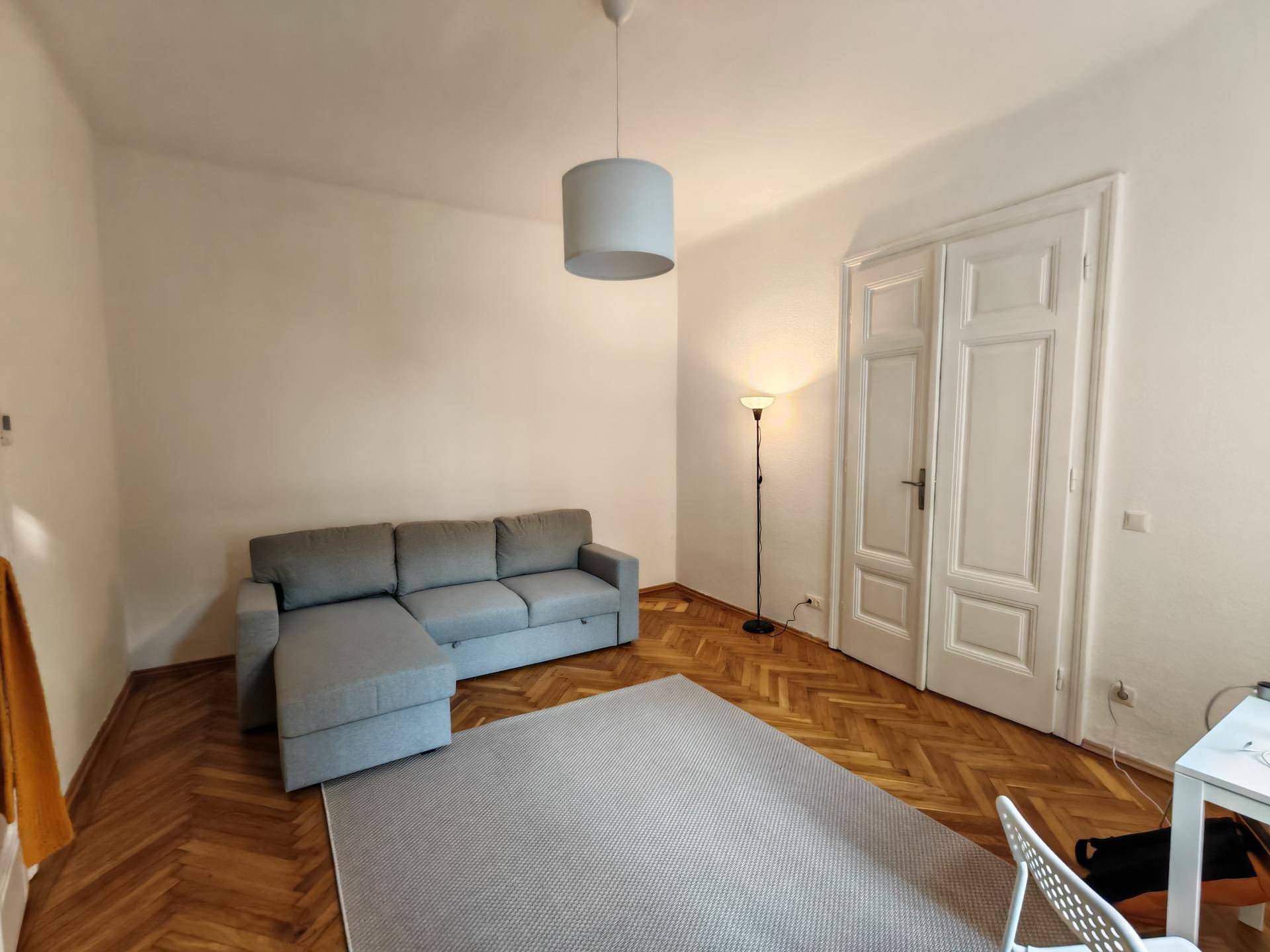 Gemütliches Wohnzimmer mit einem bequemen Ecksofa, Stehlampe und klassischem Fischgrätparkettboden.