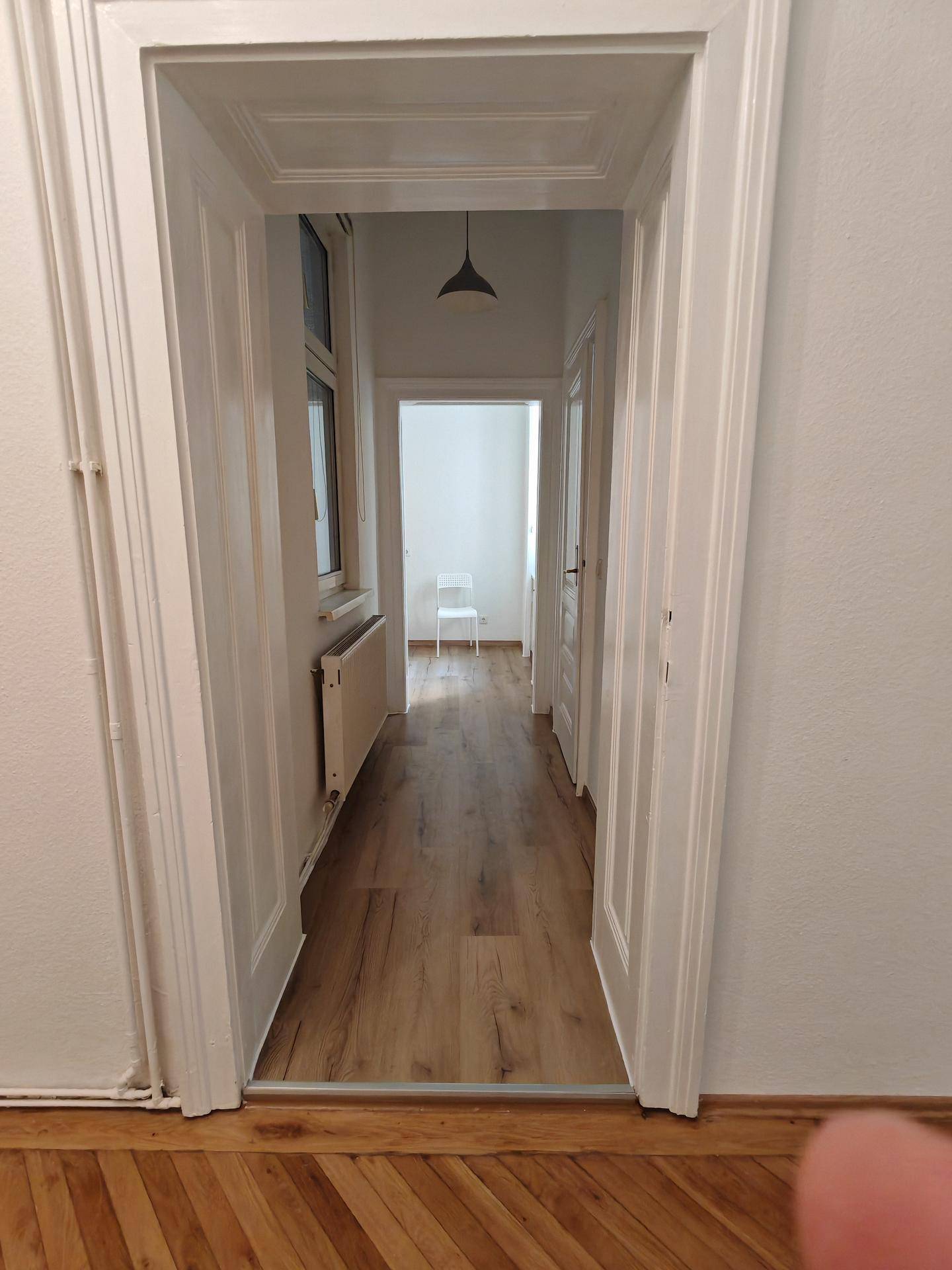 Heller Flur mit Laminatboden, einem Heizkörper unter dem Fenster und Zugang zu weiteren Räumen.