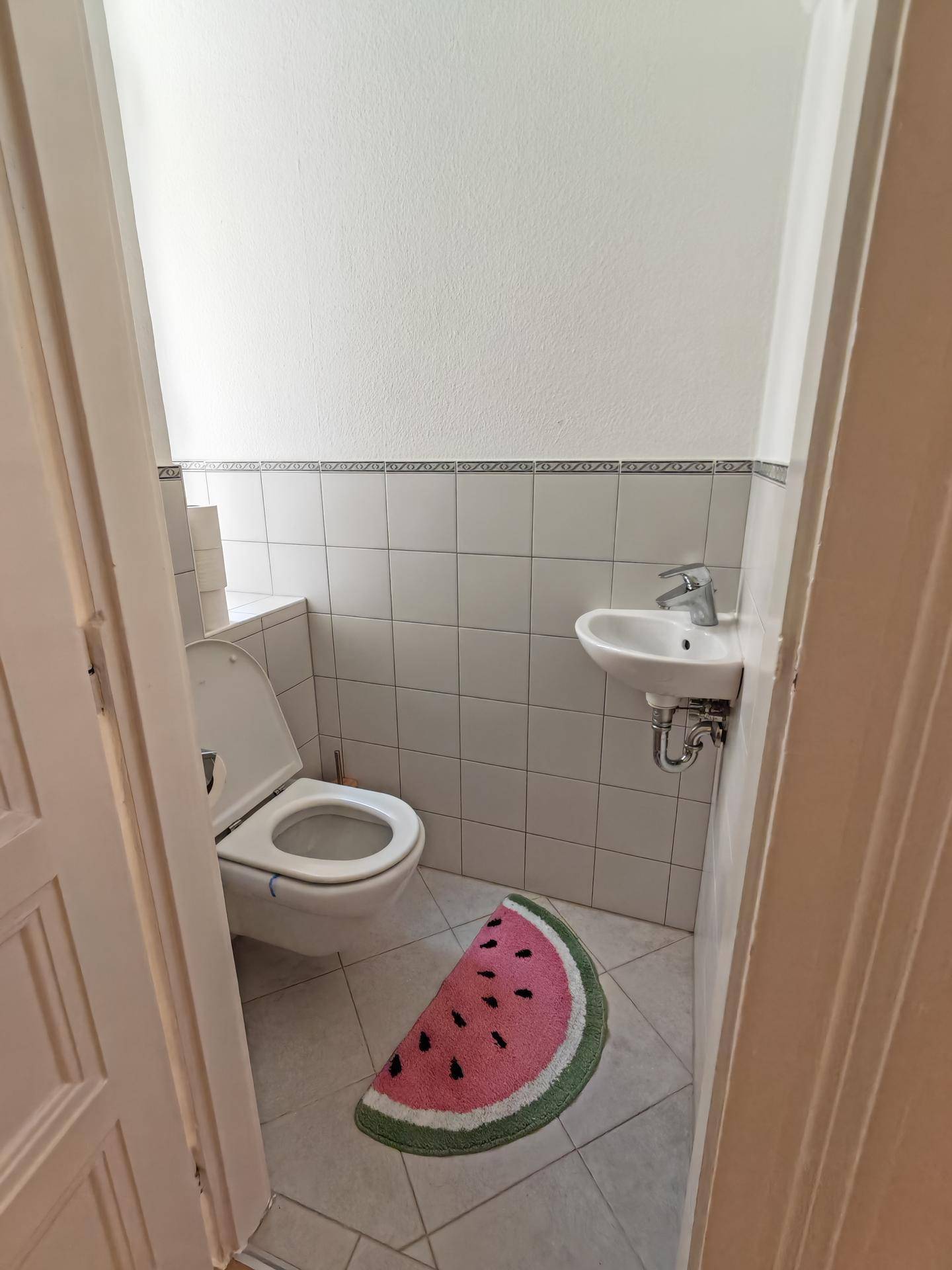 Kleines Gäste-WC mit weiß gefliesten Wänden, einem Wand-WC und einem dekorativen Teppich.