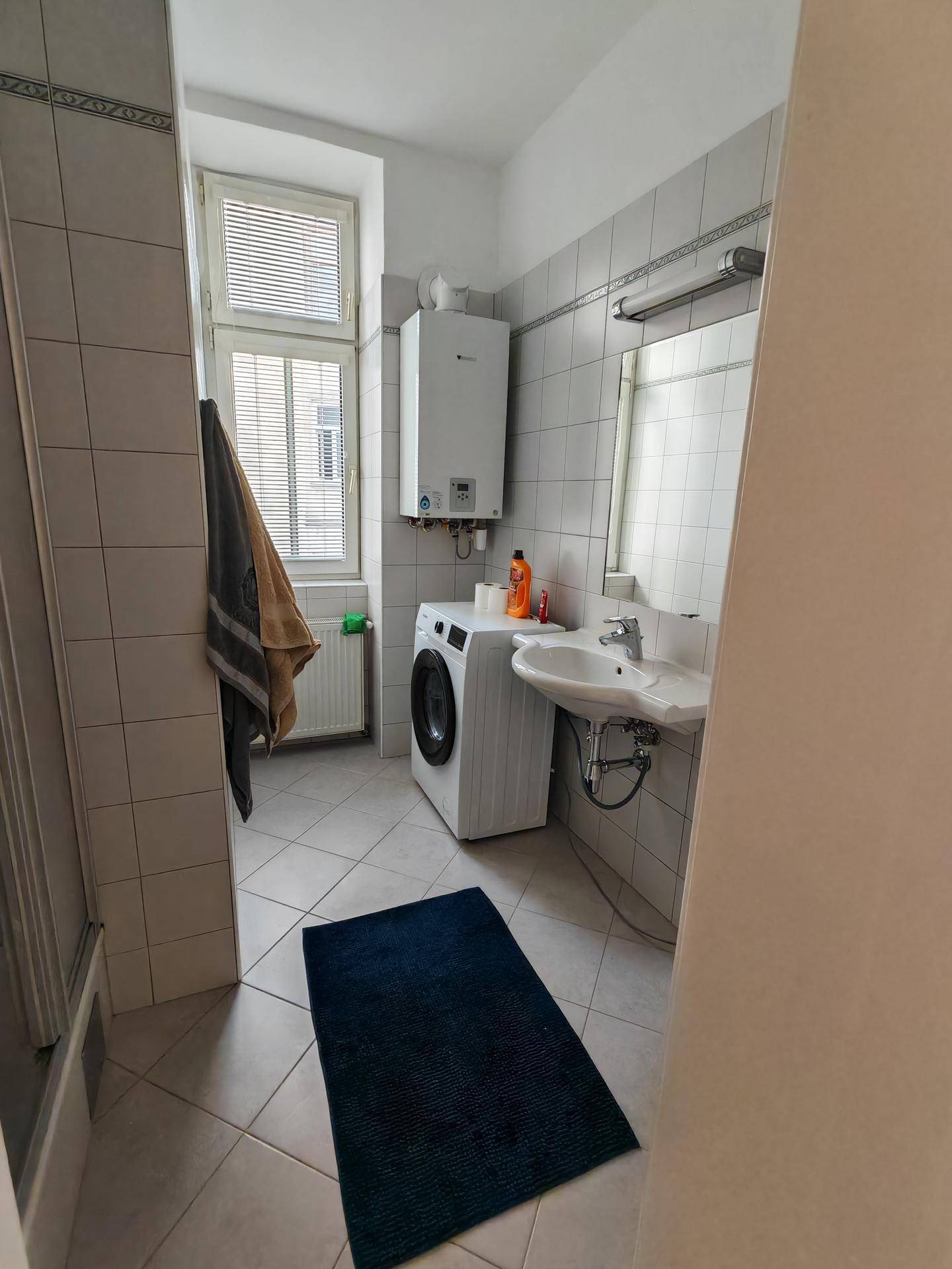 Funktionales Badezimmer mit Waschbecken, Waschmaschine, Warmwasserbereiter und Fenster.
