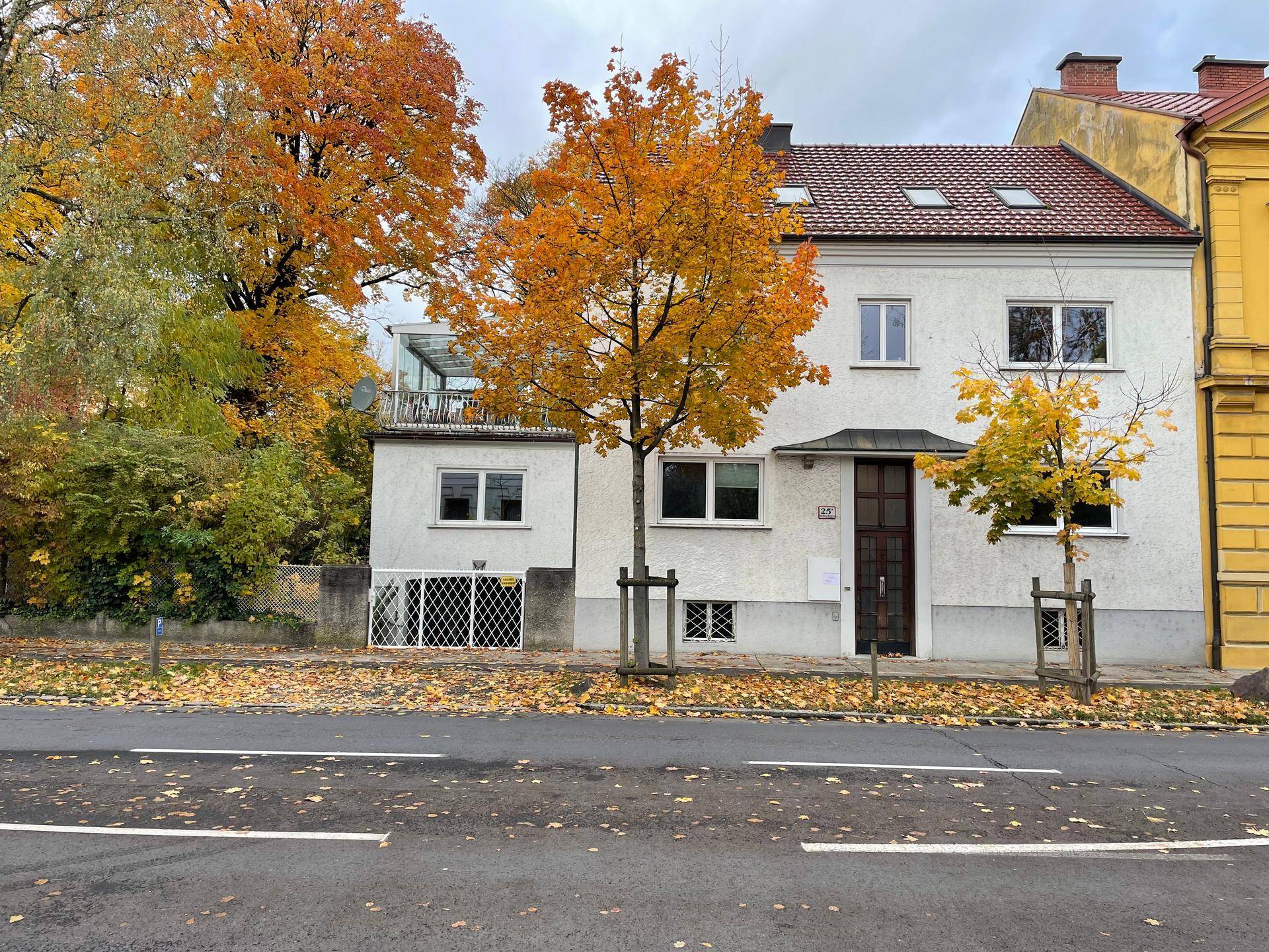 Weißes Wohnhaus mit herbstlichen Bäumen davor und einer verglasten Loggia auf dem Dachgeschoss.