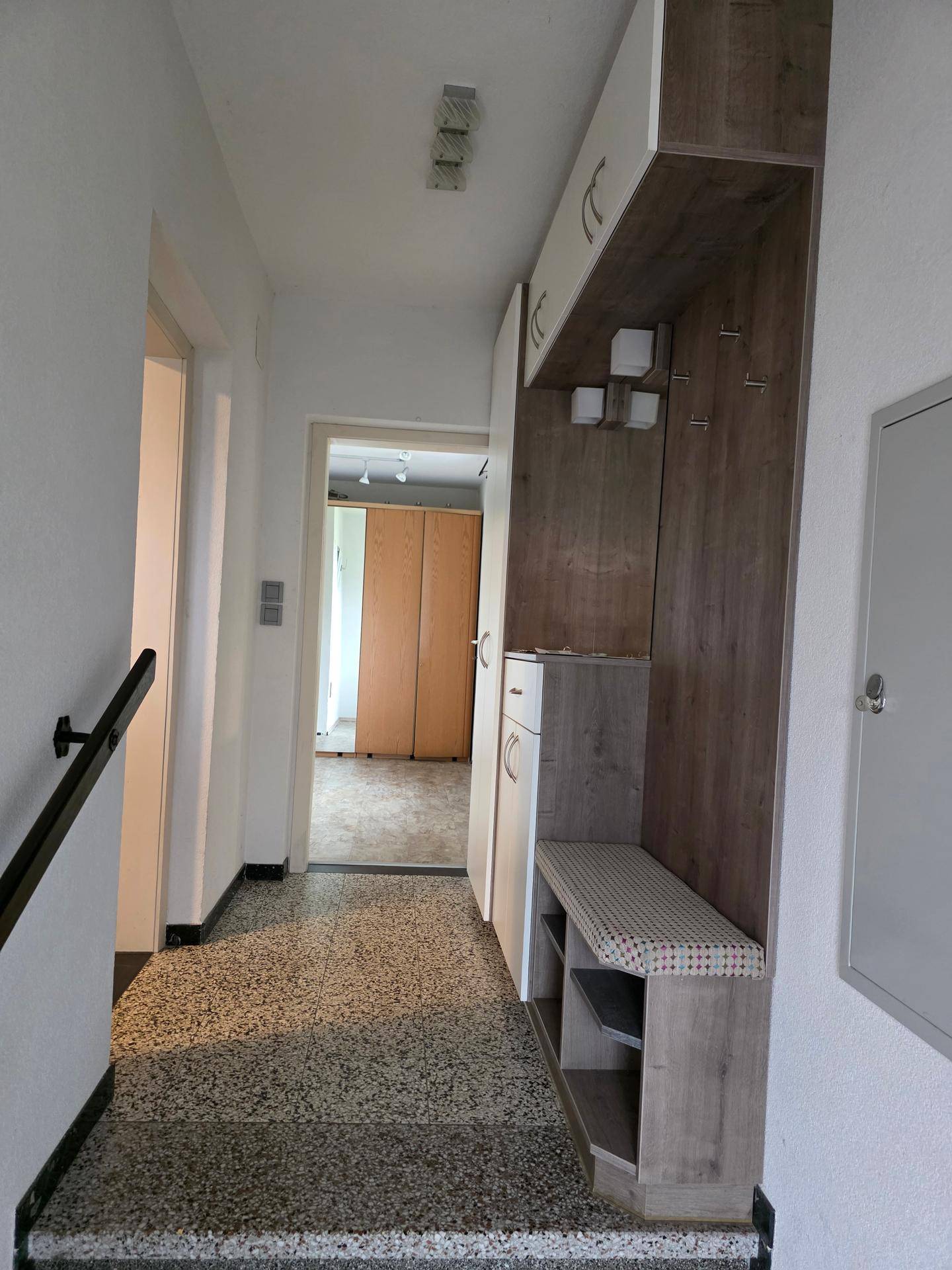 Heller Flur mit Terrazzoboden und praktischer Garderobe mit integrierter Sitzbank.