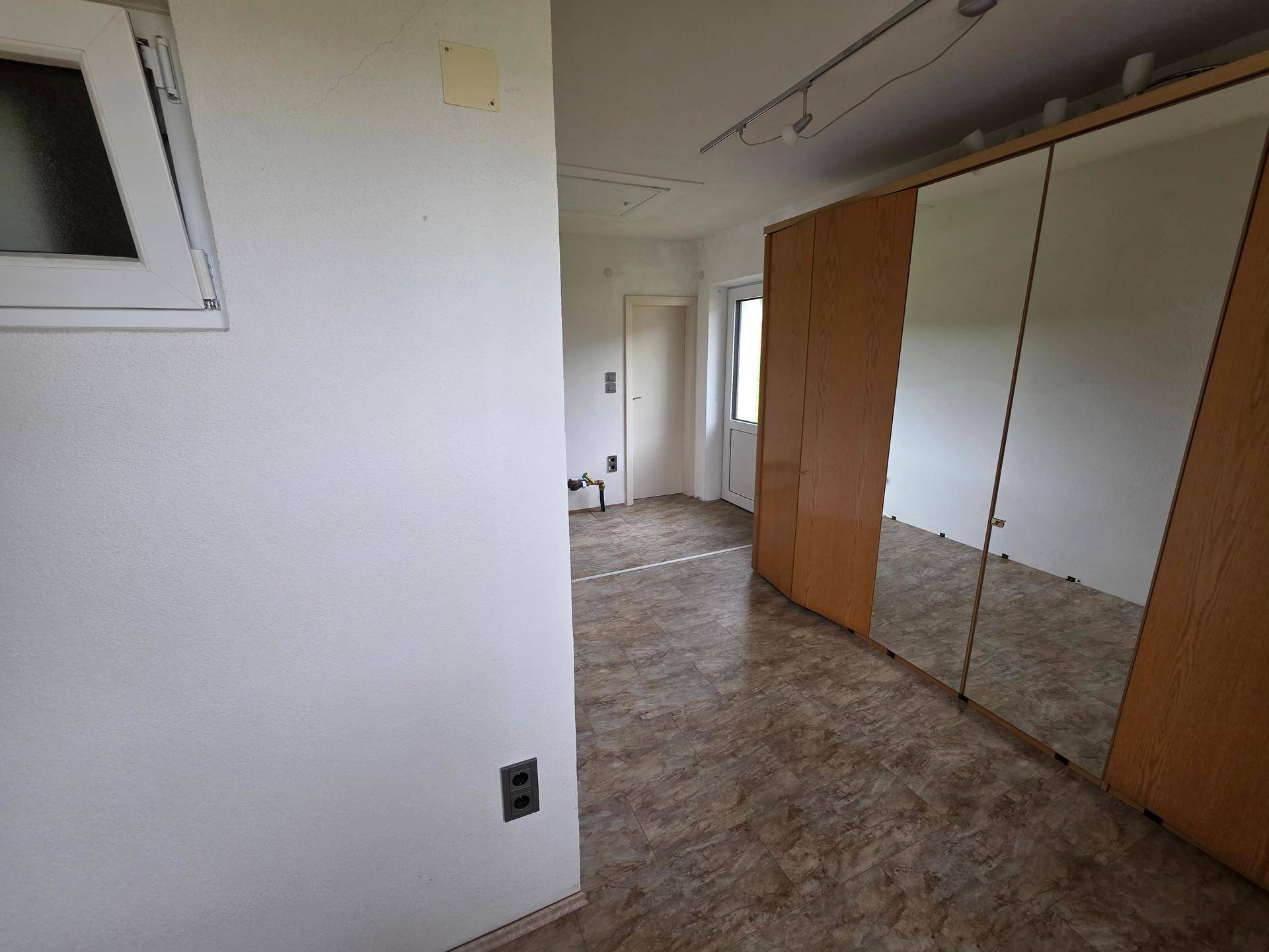 Leeres Zimmer mit großem Spiegelschrank, Fenster und hellem Bodenbelag, bereit zur individuellen Gestaltung.