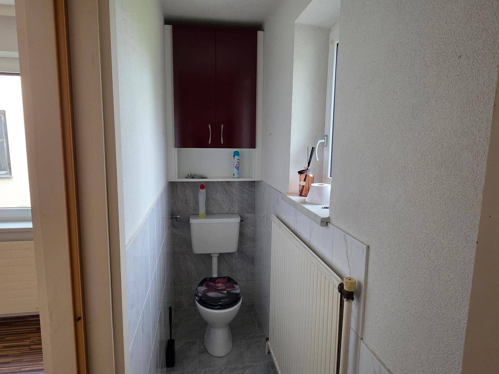 Kleines WC mit Toilette, Fliesen an den Wänden und einem Fenster für natürliche Belüftung.