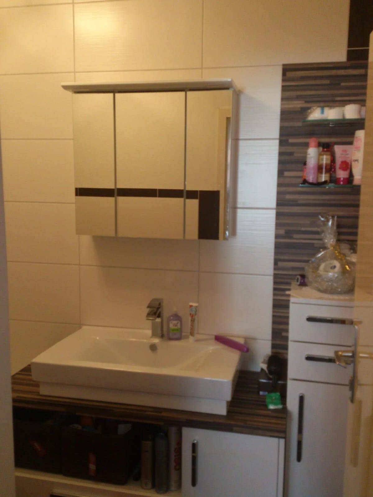 Badezimmer mit modernem Waschbecken, Spiegelschrank und beigefarbenen Fliesen mit braunen Akzenten.