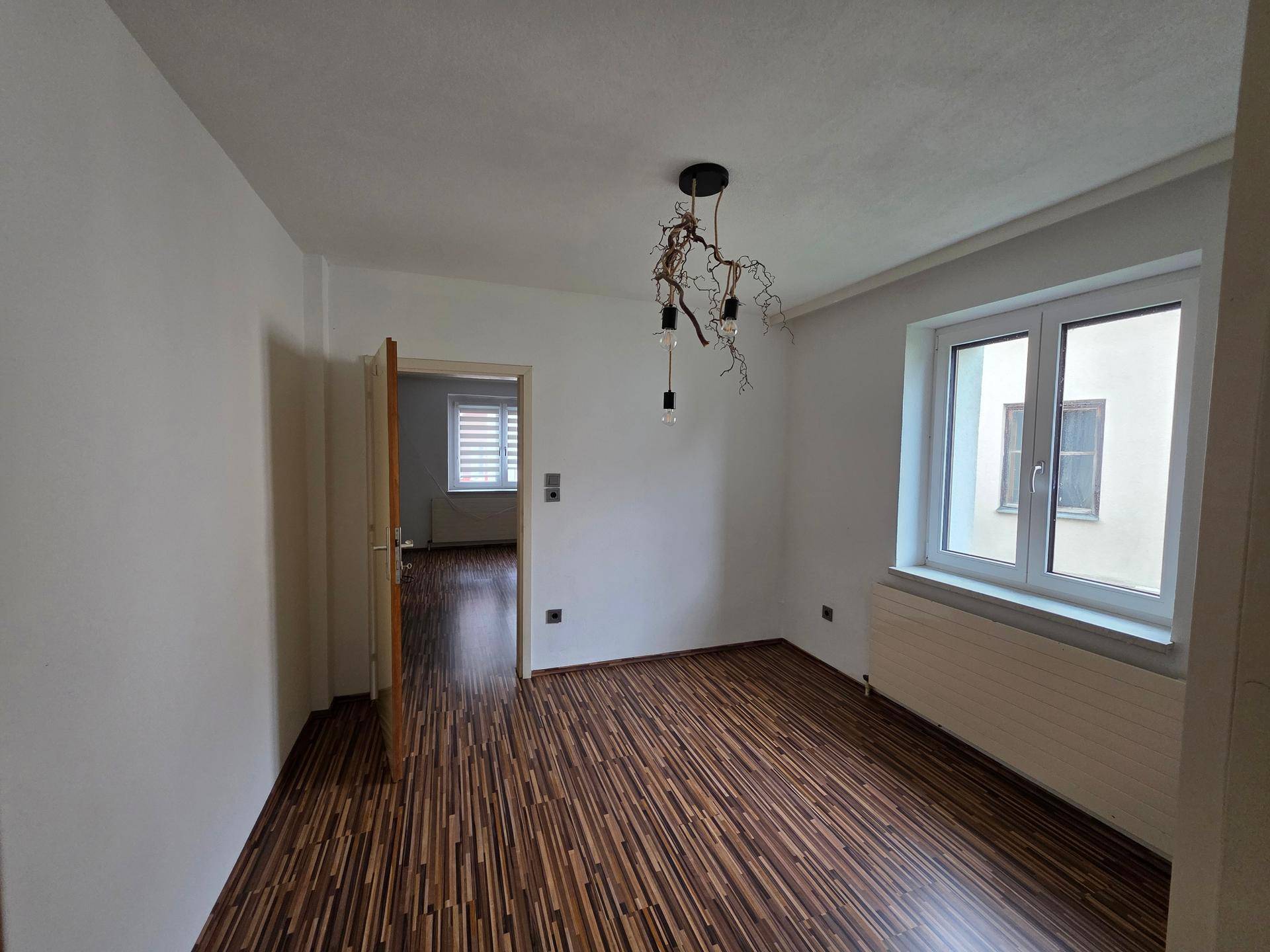 Helles Zimmer mit Laminatboden und dekorativer Deckenleuchte, mit Blick in einen angrenzenden Raum.