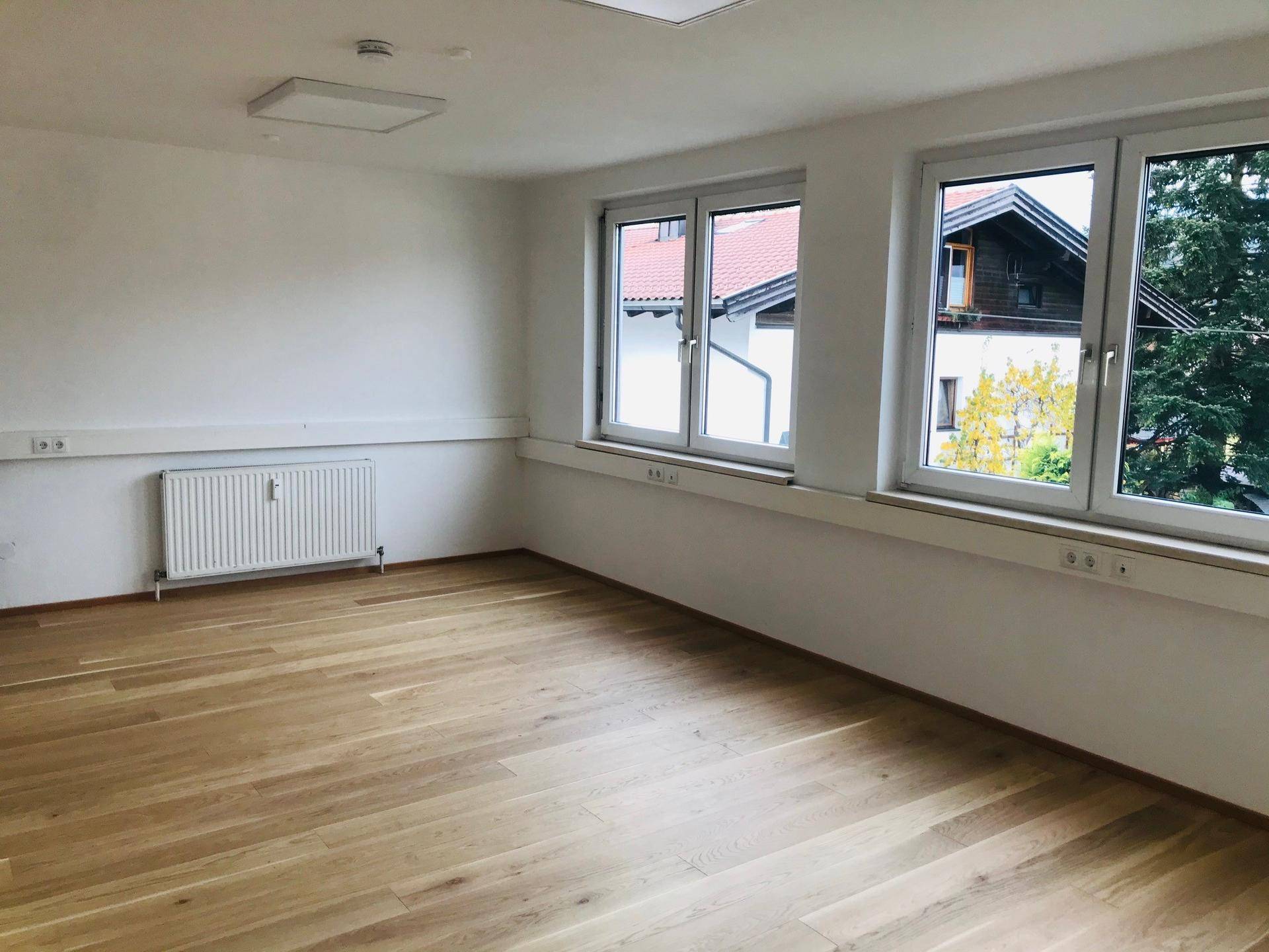 Leerer, heller Raum mit Holzfußboden und großen Fenstern, bereit zur individuellen Gestaltung.