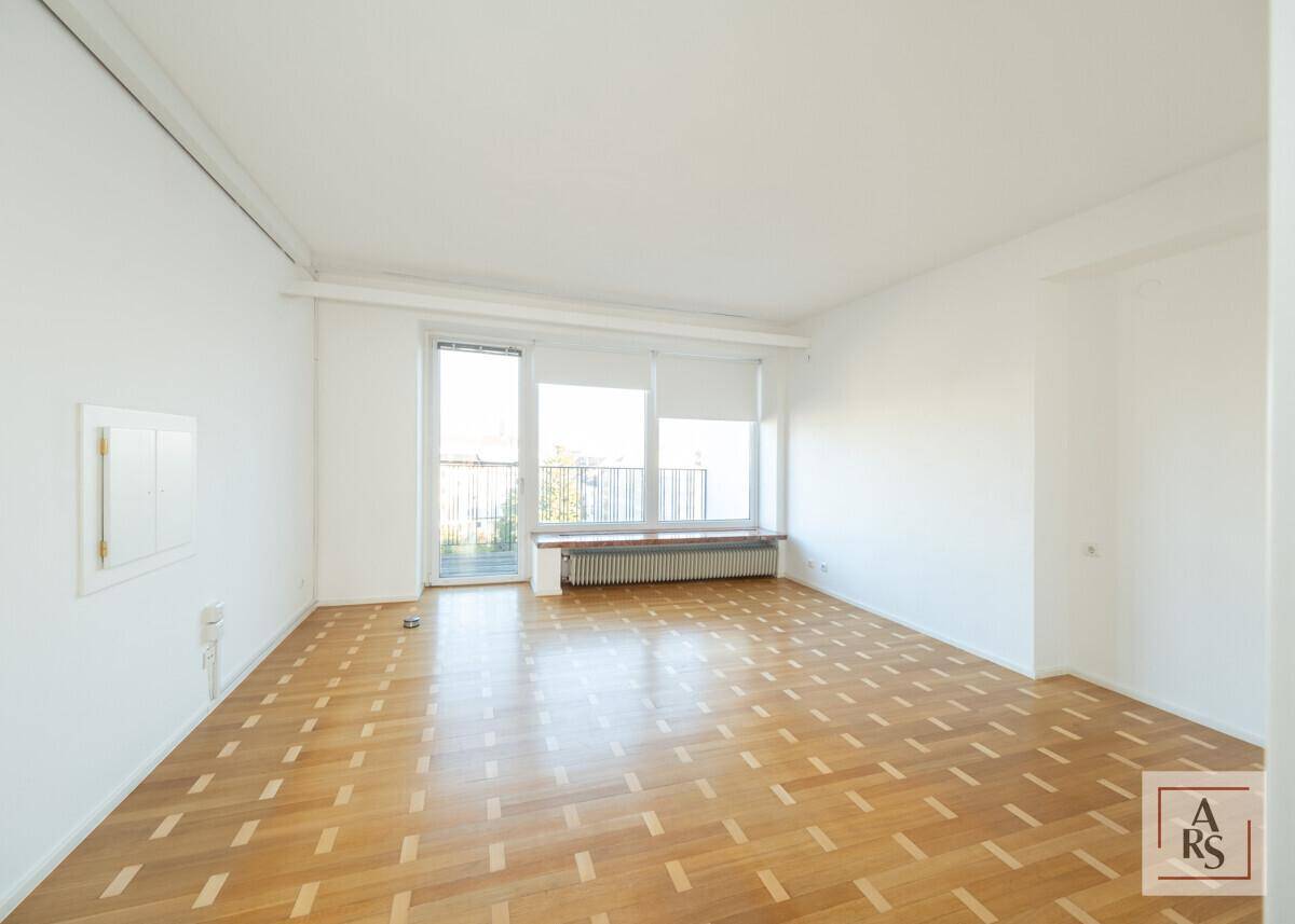 Geräumiges Wohnzimmer mit Fischgrätparkett, großen Fenstern und Blick ins Grüne.