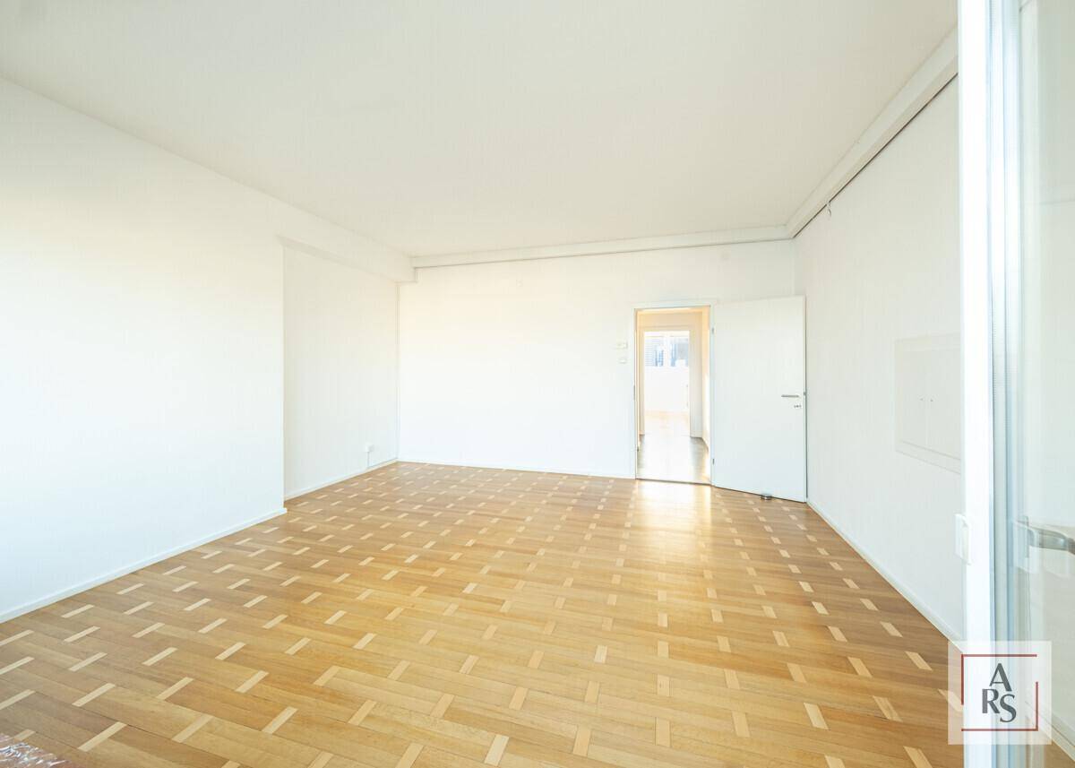 Heller Wohnbereich mit klassischem Parkettboden und Zugang zu einem weiteren Raum.